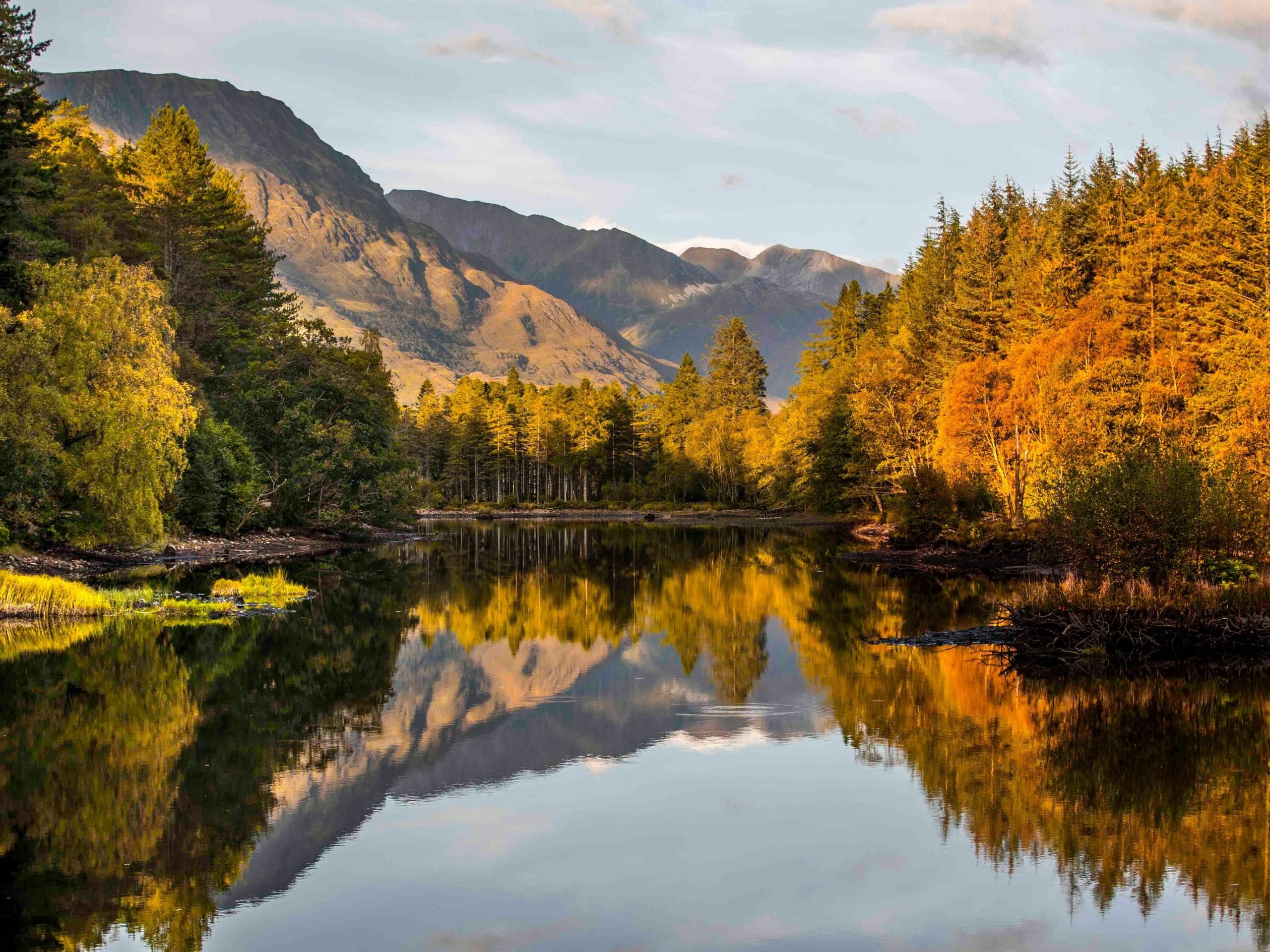 Photo of trees displaying autumn colors reflected in the still waters of Glencoe Lochan in the Scottish Highlands, where participants are set to begin the ultra marathon.