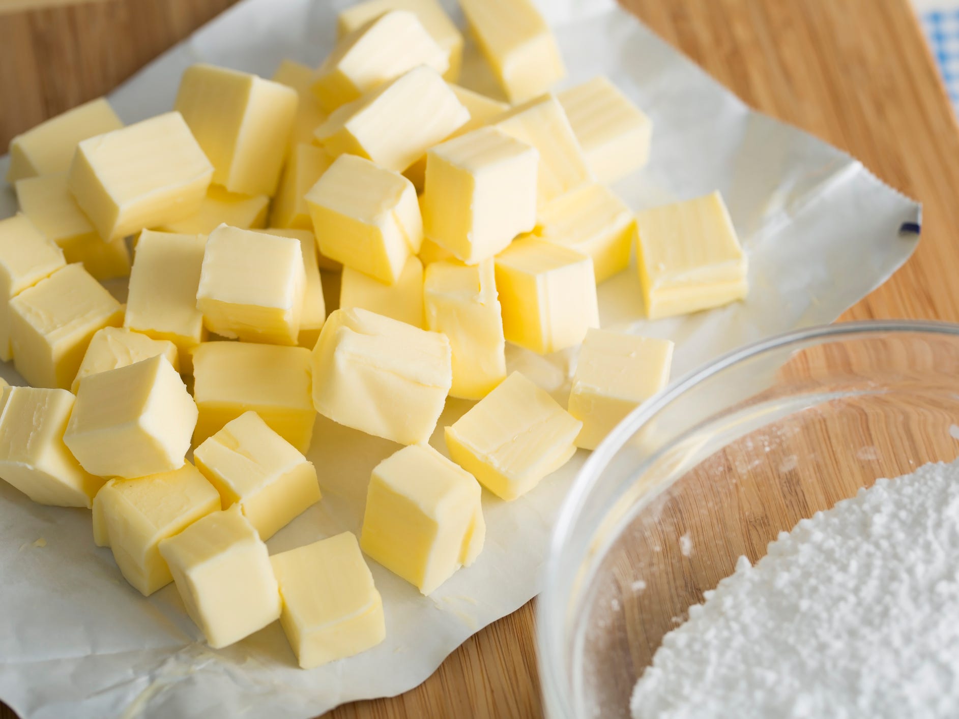 Cubed butter sitting on the butter wrapper next to a bowl of flour