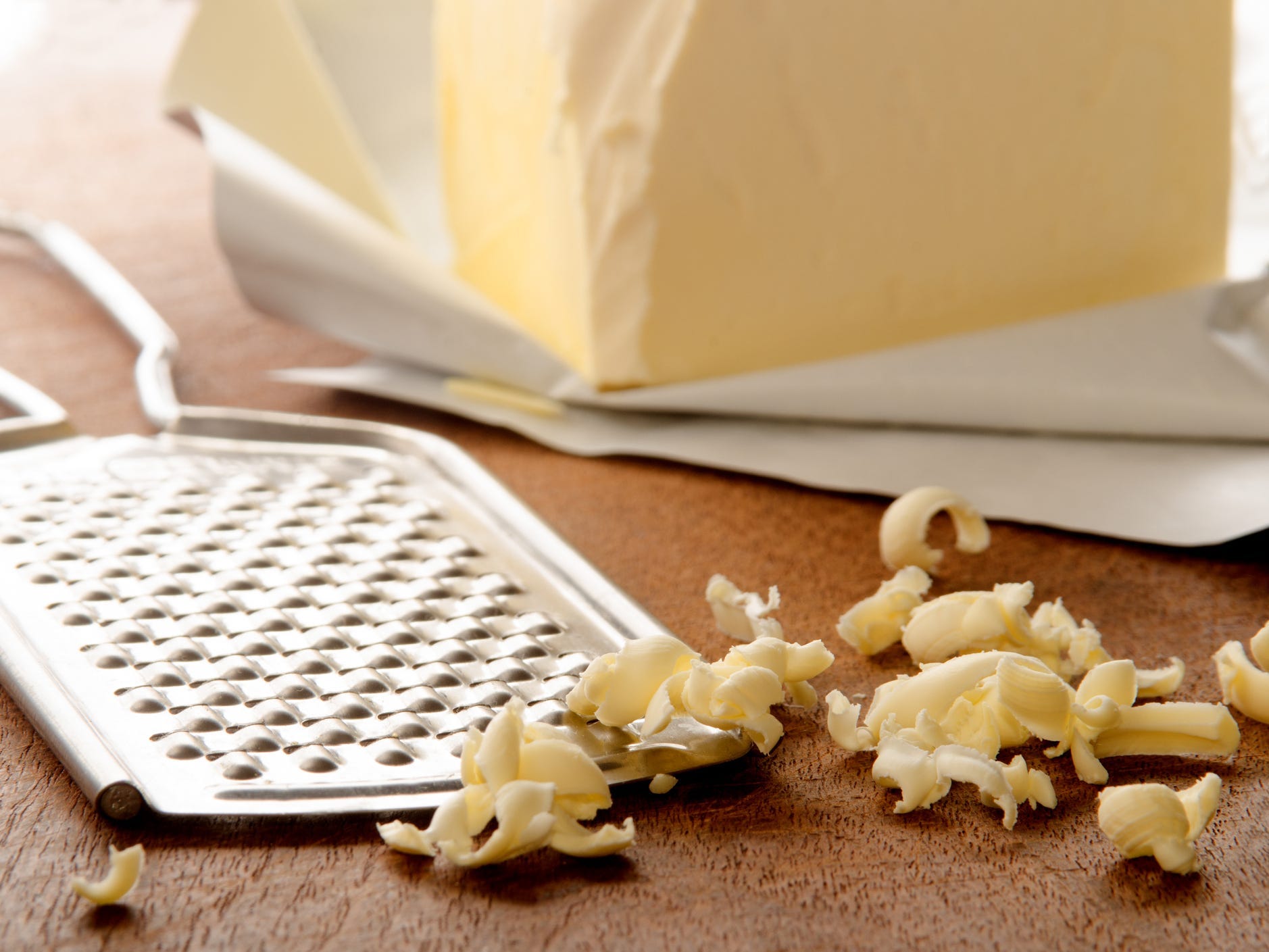 Grated butter shreds next to a handheld grater with a block of butter in the background