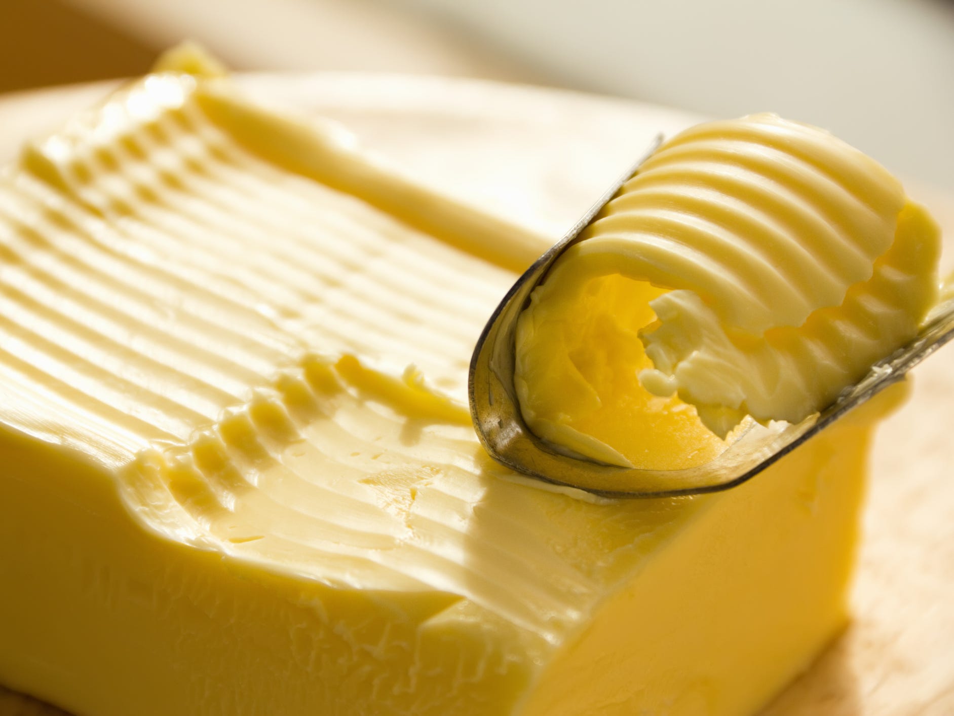 A block of butter being scraped with a butter spreading knife that's removing a curl of butter