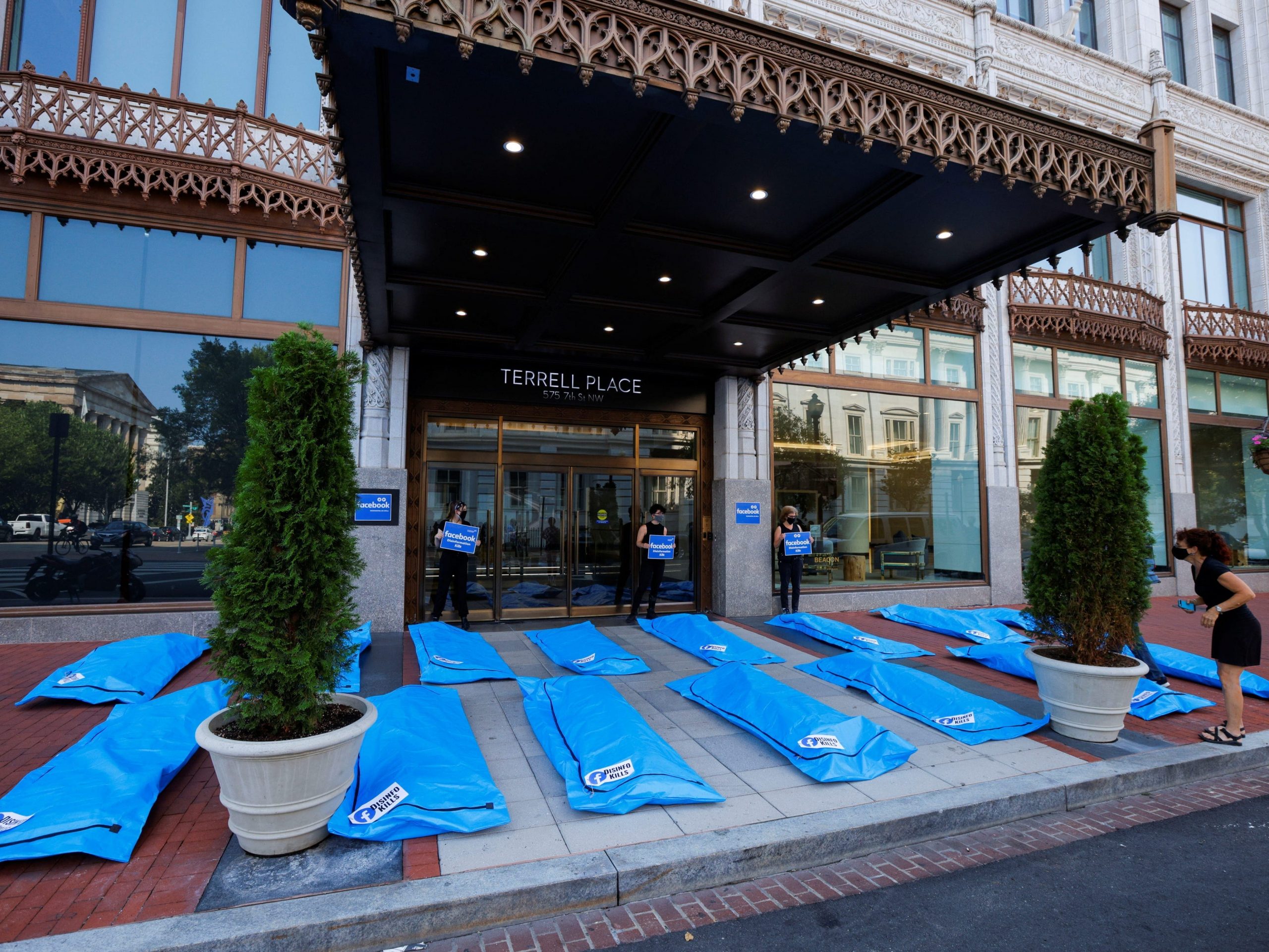 blue body bags laying on the ground outside facebook's dc office under an awning. the bags bear text that reads "disinfo kills"