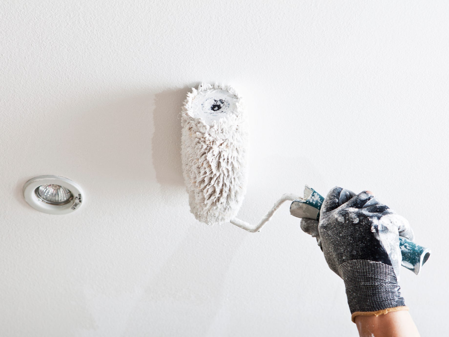 A close up of a gloved hand holding a paint roller painting a ceiling