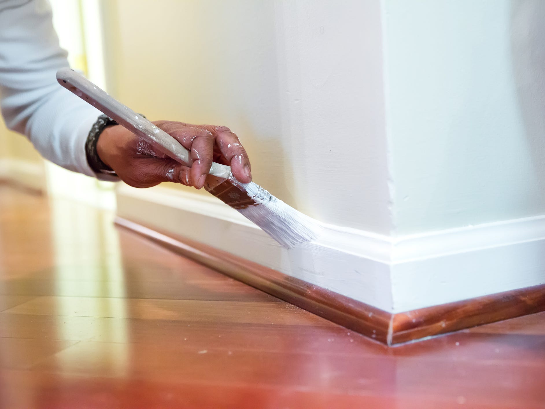 A hand holding a paintbrush and painting the baseboards