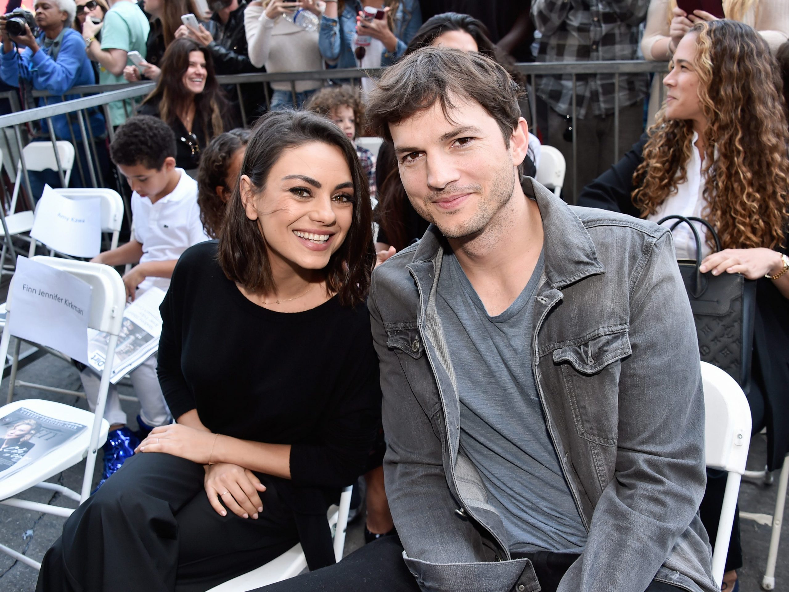 Mila Kunis and Ashton Kutcher leaning toward each other and smiling.