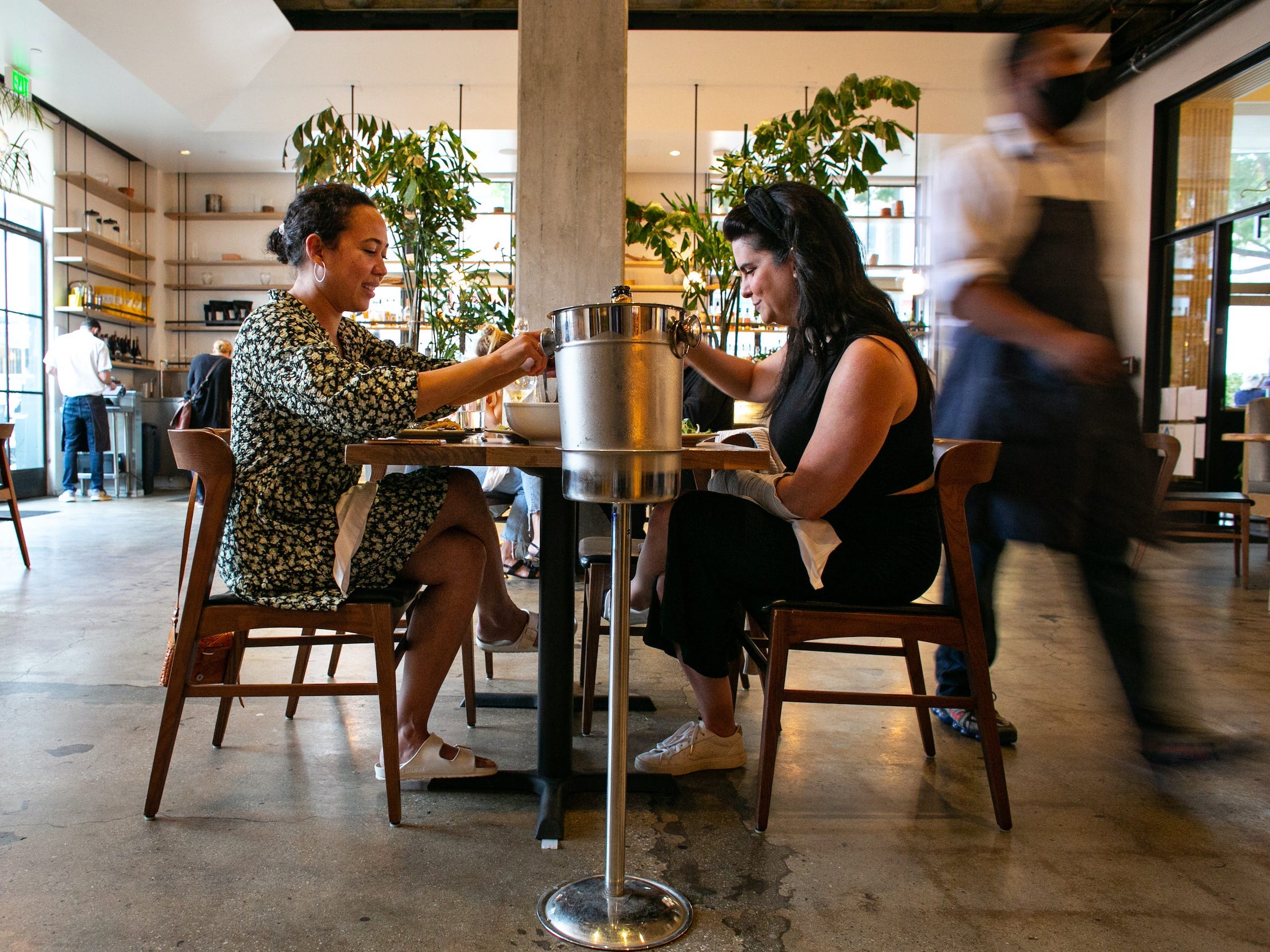 Two women dine across from each other indoors at a restaurant while server walks behind them