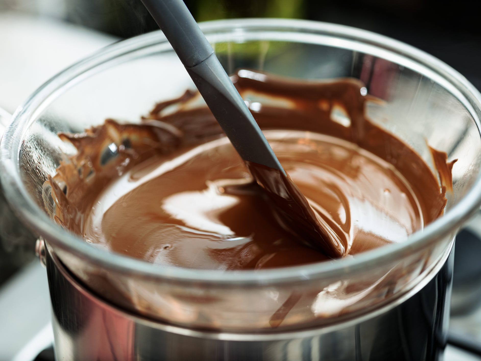 A glass bowl of melted chocolate sitting on top of a saucepan.