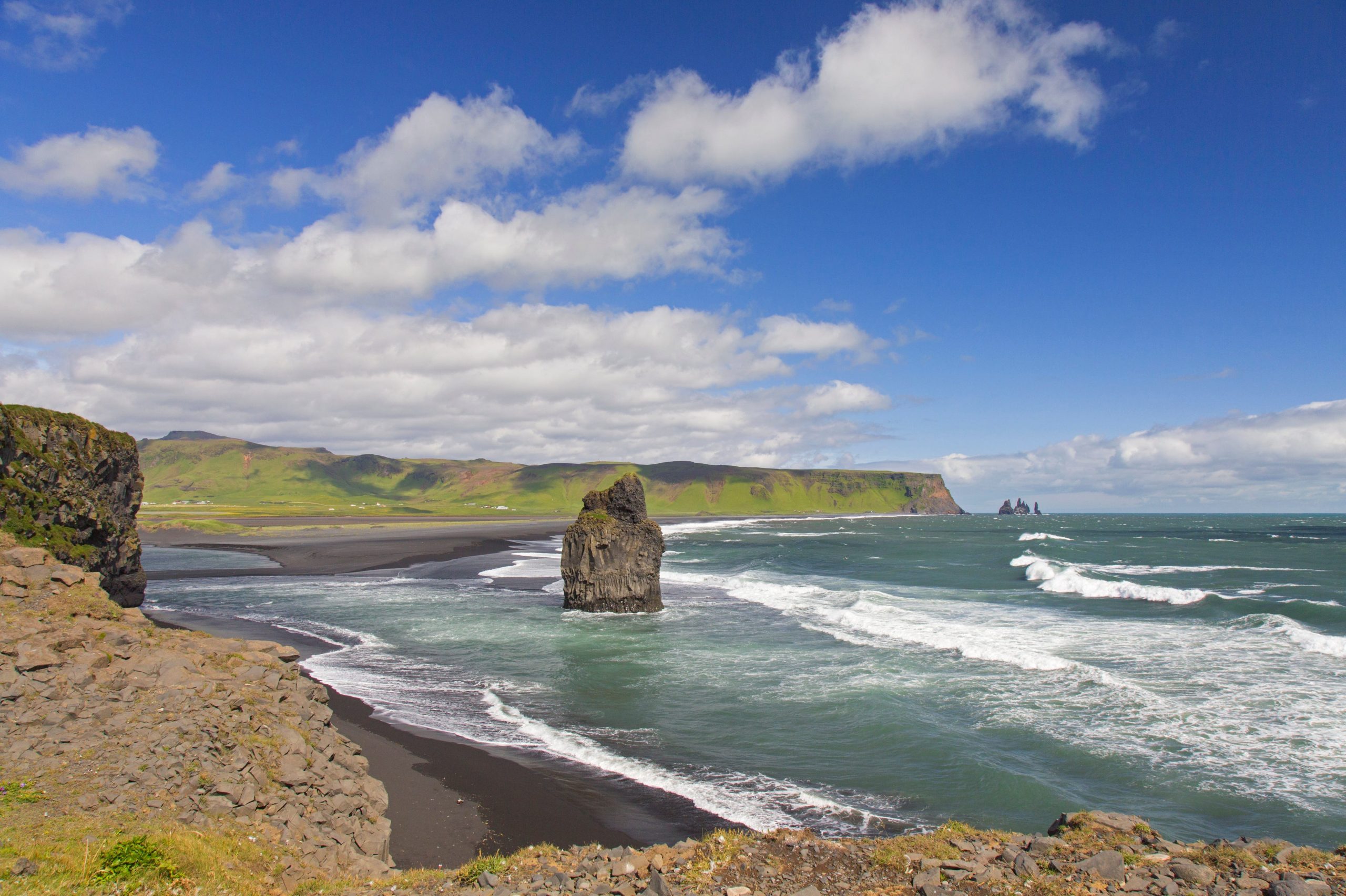 A big rock juts out from the ground in the sea along a beach in Iceland