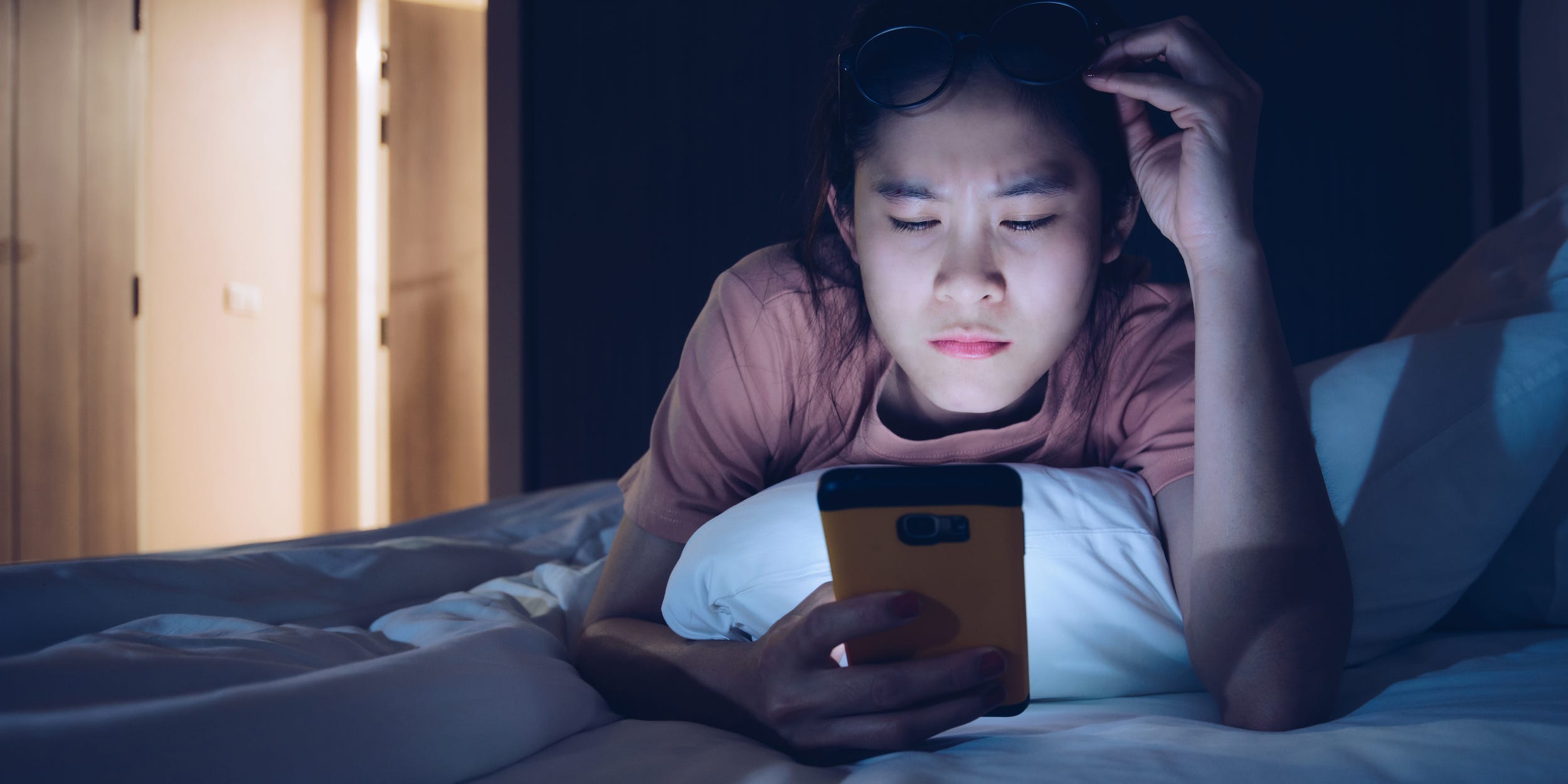 Teen using smartphone in bed at night dark