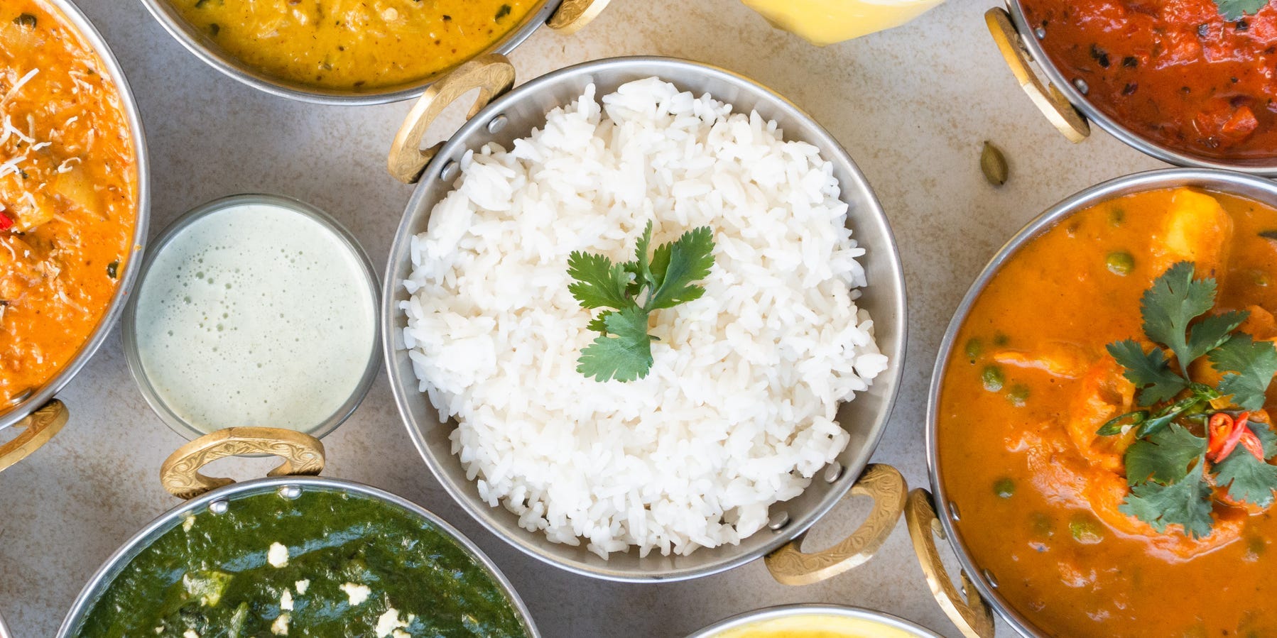 A bowl of cooked basmati rice surrounded by other bowls of Indian curries and dishes