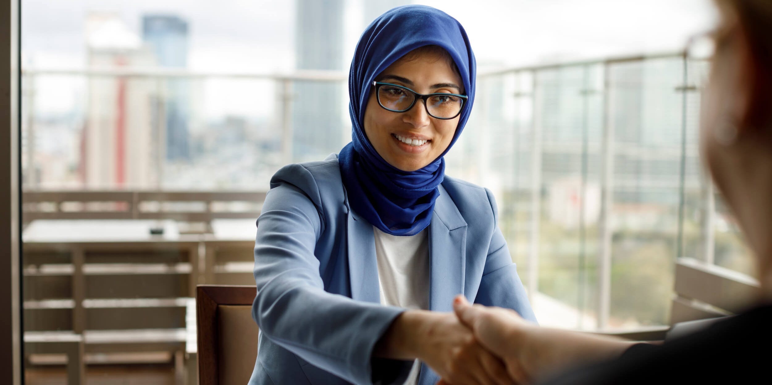 Smiling muslim woman in a business meeting shaking someone’s hand.