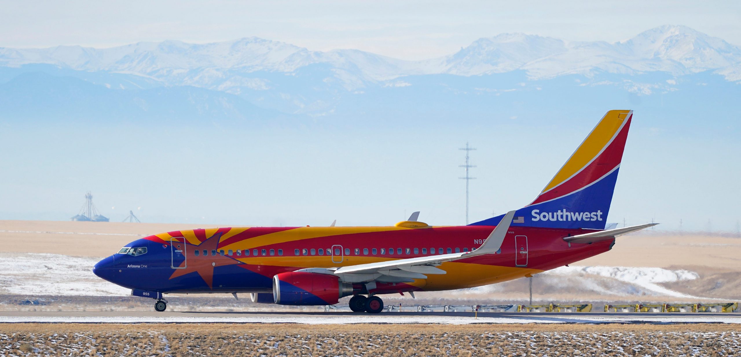 A Southwest Airlines plane painted with Arizona's flag on a runway in front of snow-tipped mountains