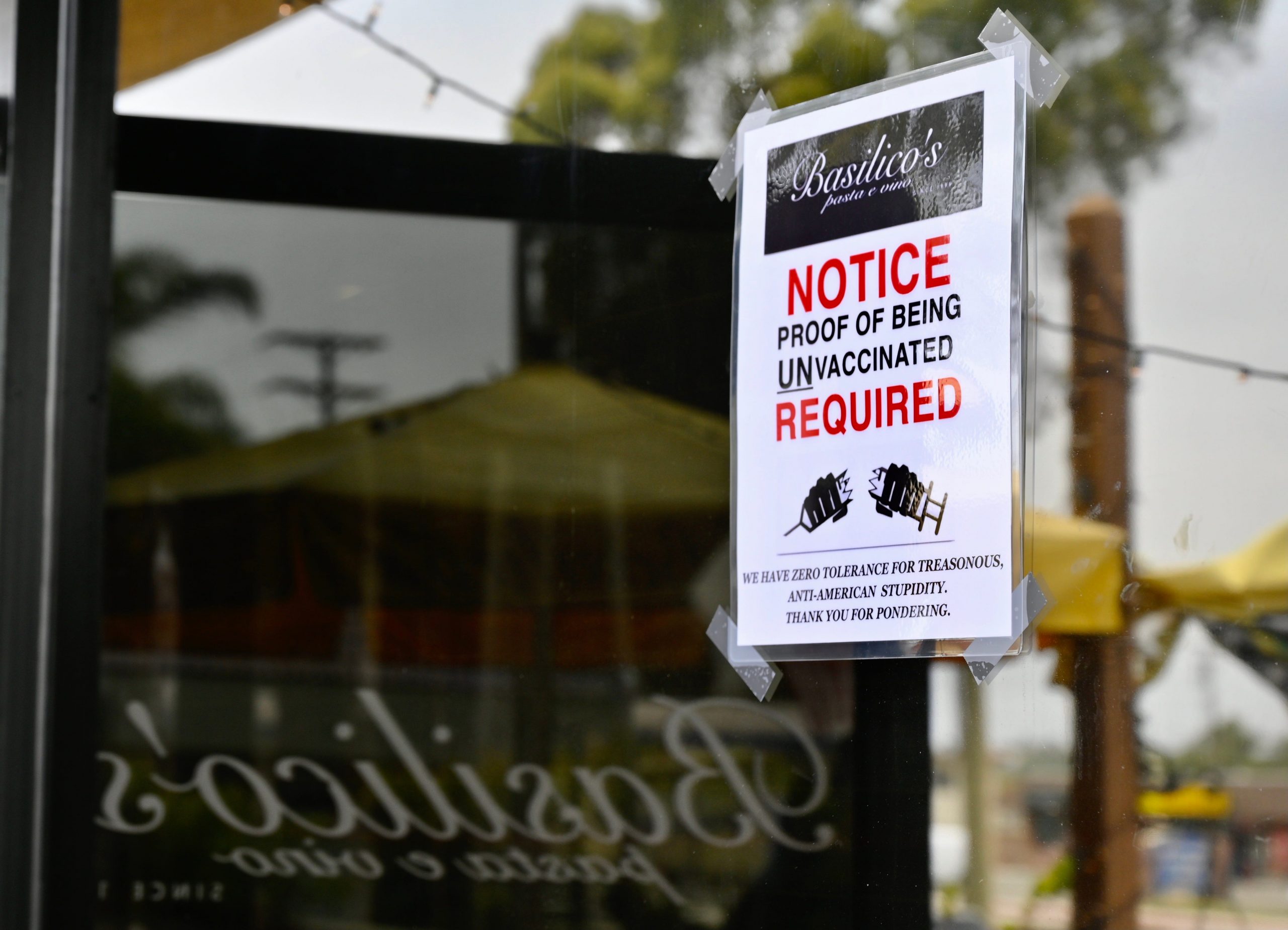 A sign taped to the window of California restaurant Basilicos Pasta e vino says they require "proof of being unvaccinated."