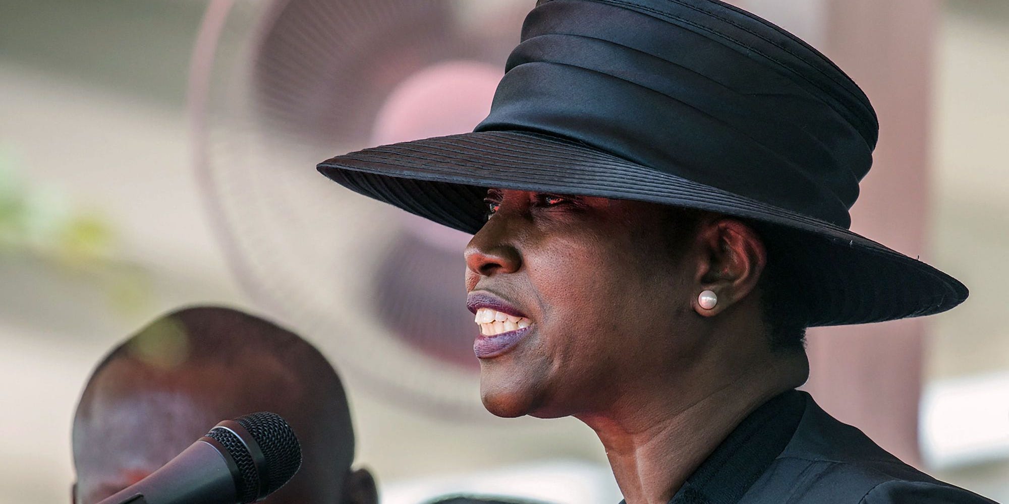 Martine Moïse, wearing a black hat, speaks at a microphone