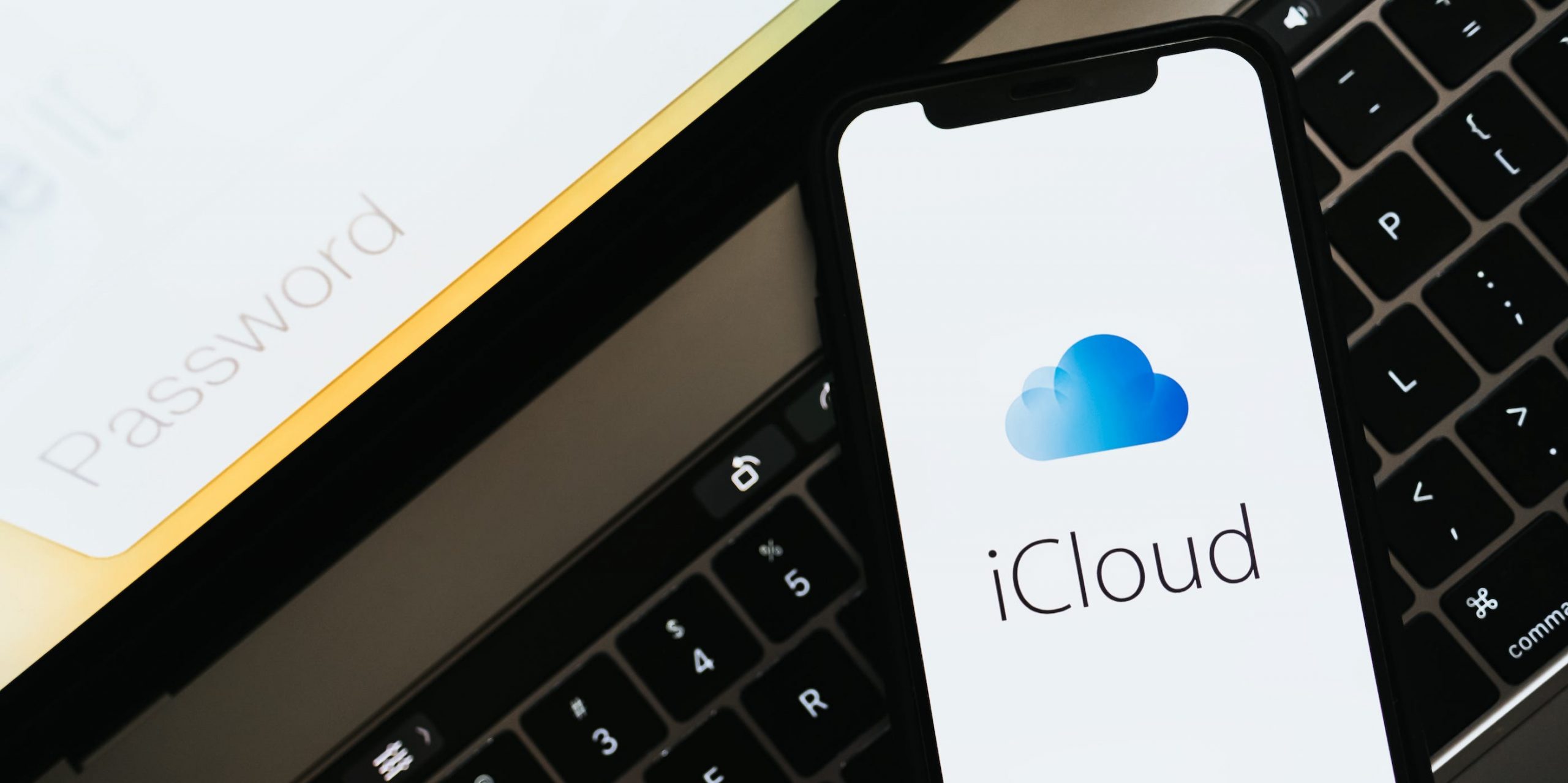 An iPhone displaying the iCloud logo, laid on top of a MacBook.