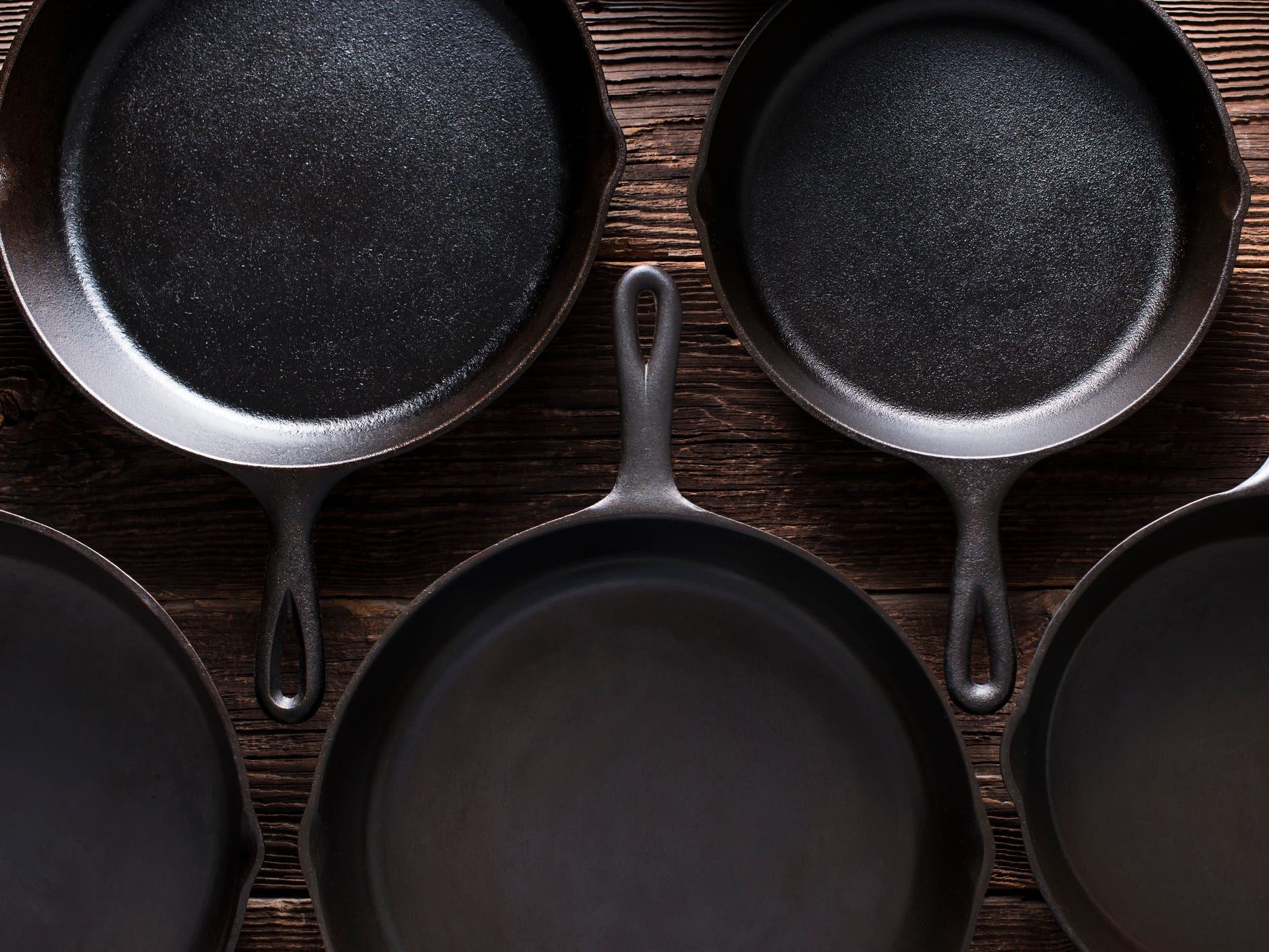 Five cast iron skillets against a dark wood background.