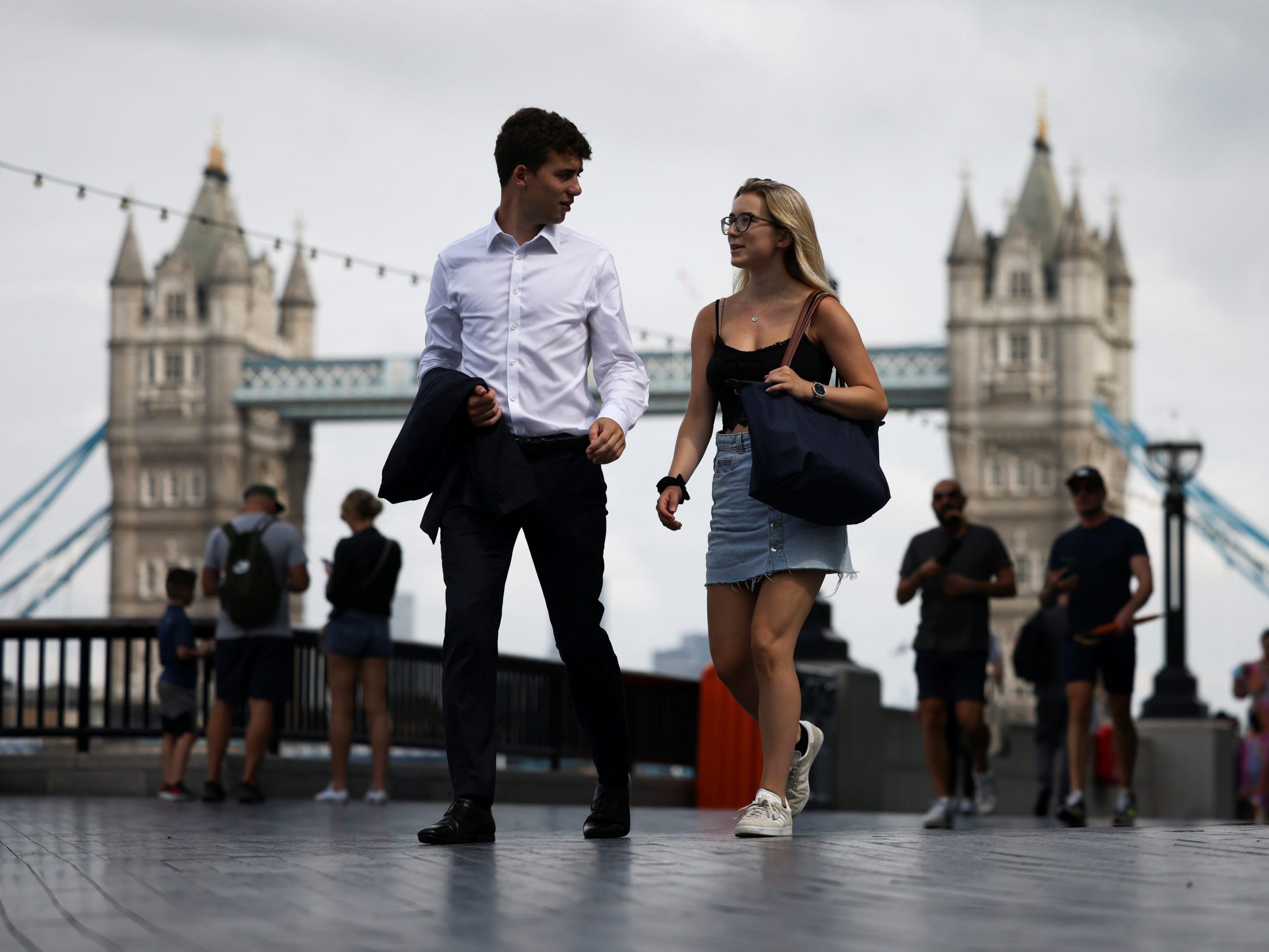 couple man woman walking along river thames in london with tower bridge in background