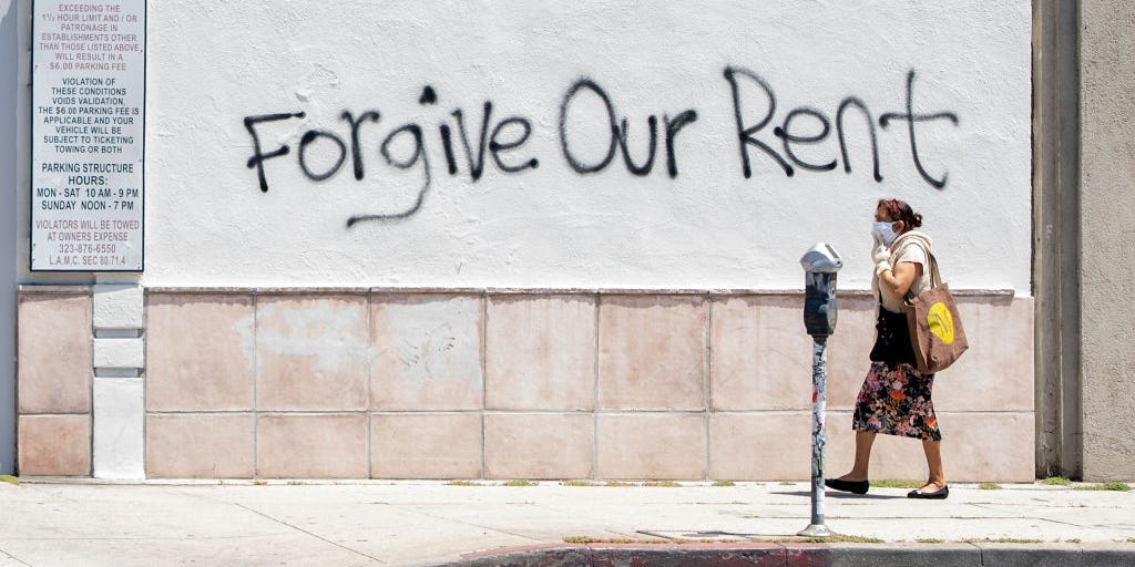 A woman walks past a wall in Los Angeles that has graffiti reading "Forgive Our Rent"