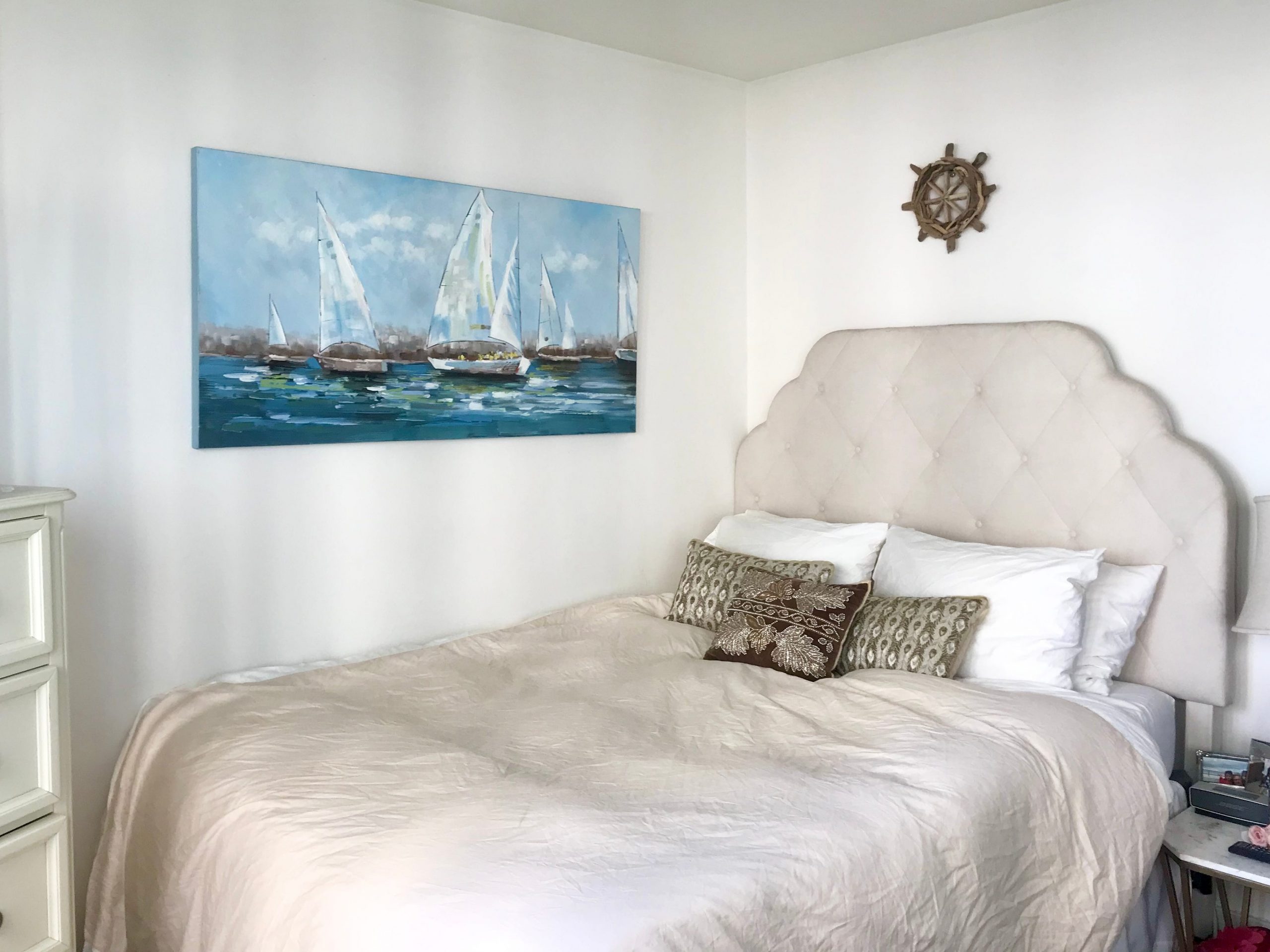 The writer's bed with a beige, quilted headboard and simple ocean painting next to it.