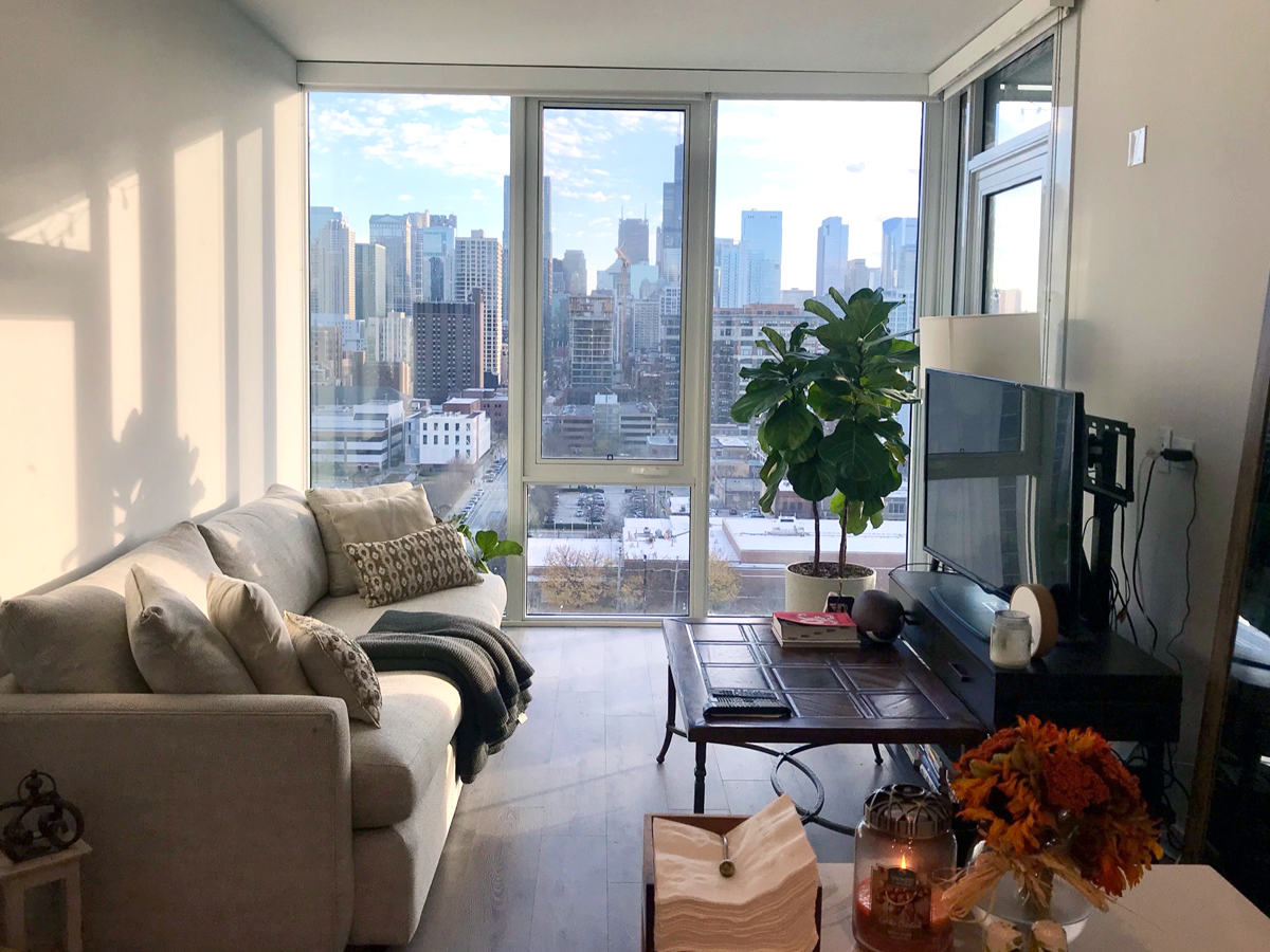 An apartment with floor-to-ceiling windows, a gray couch, and big coffee table