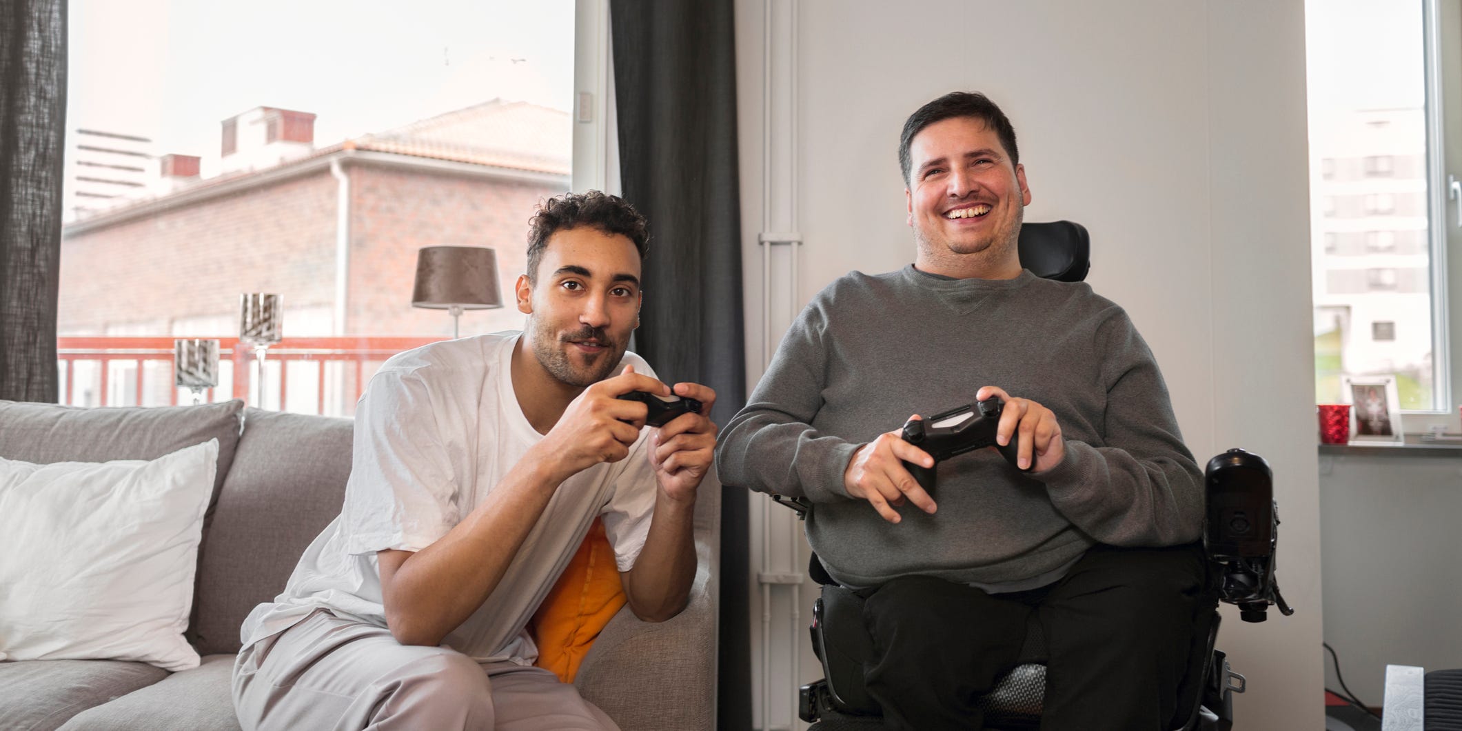 a gamer sits on the couch while another game sits in a wheelchair playing console games