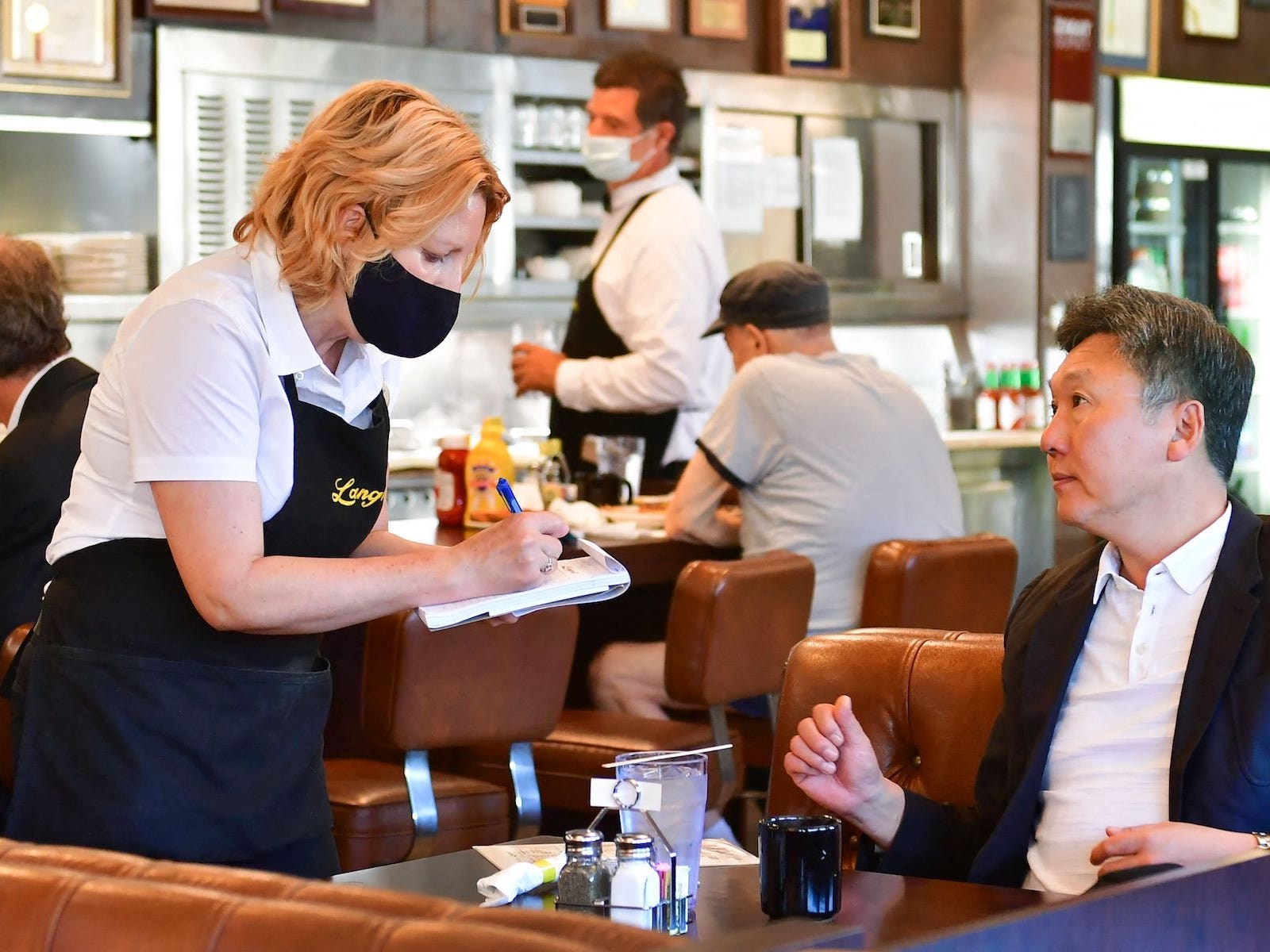 A waitress is taking a customer’s order at a table. There are other customers and another server in the background.