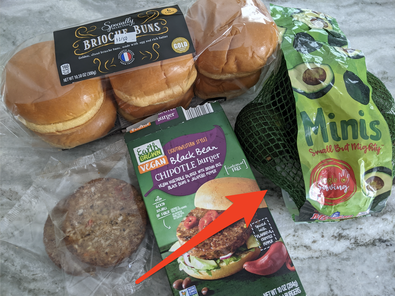 Brioche buns, veggies burgers, and a bag of mini avocados from Aldi on a gray countertop