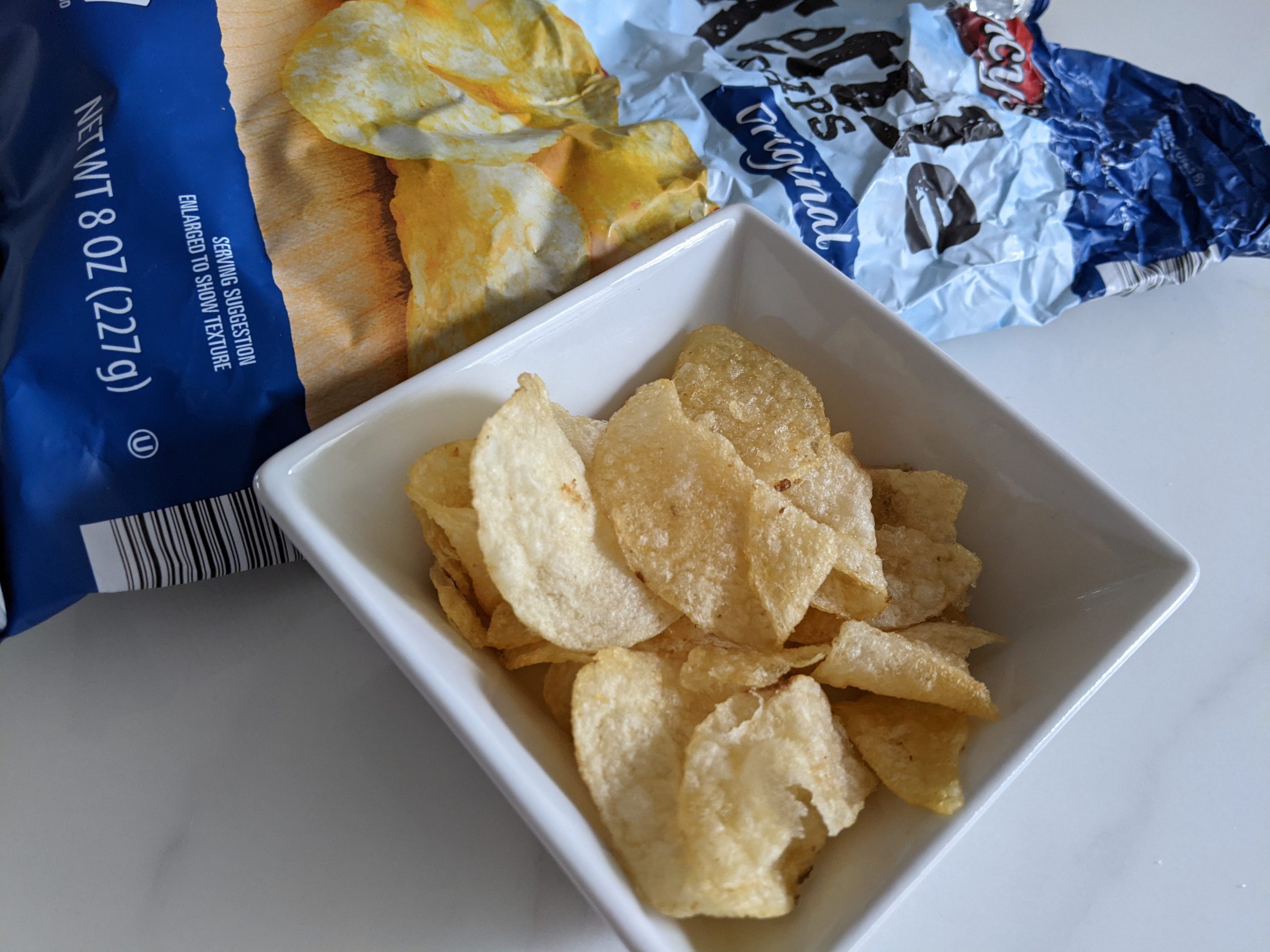 Aldi kettle chips in a small white bowl with the blue original bag in the back