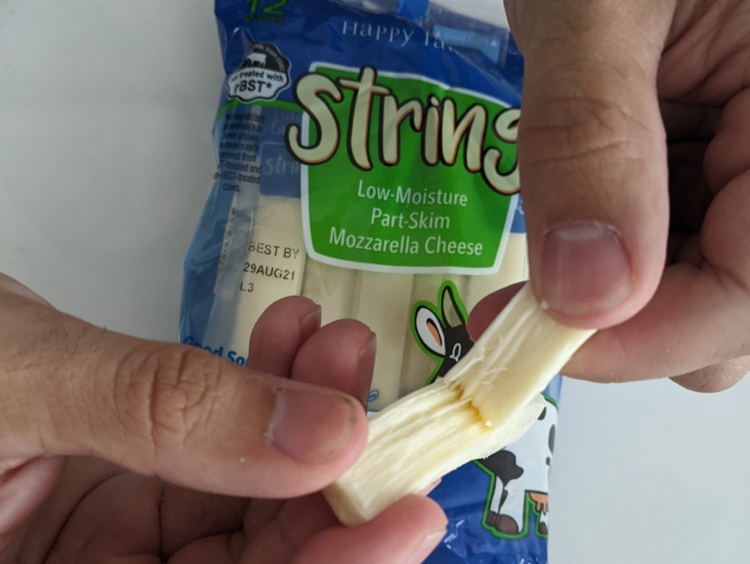 hands pulling Aldi string cheese apart with the blue and green packaging in the background