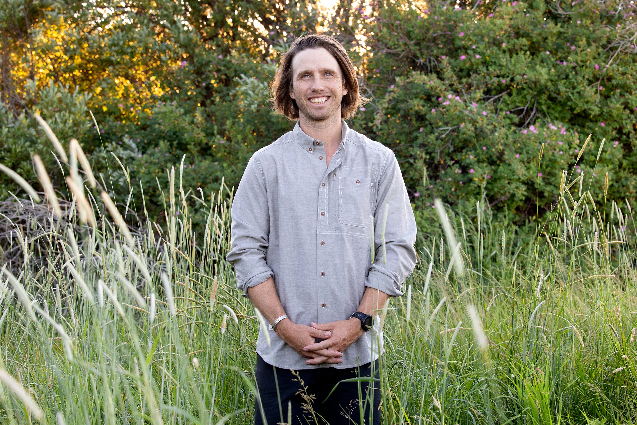 Ecologist Charles Post wears a gray button-up shirt with black shorts and smiles while posing in an open field.