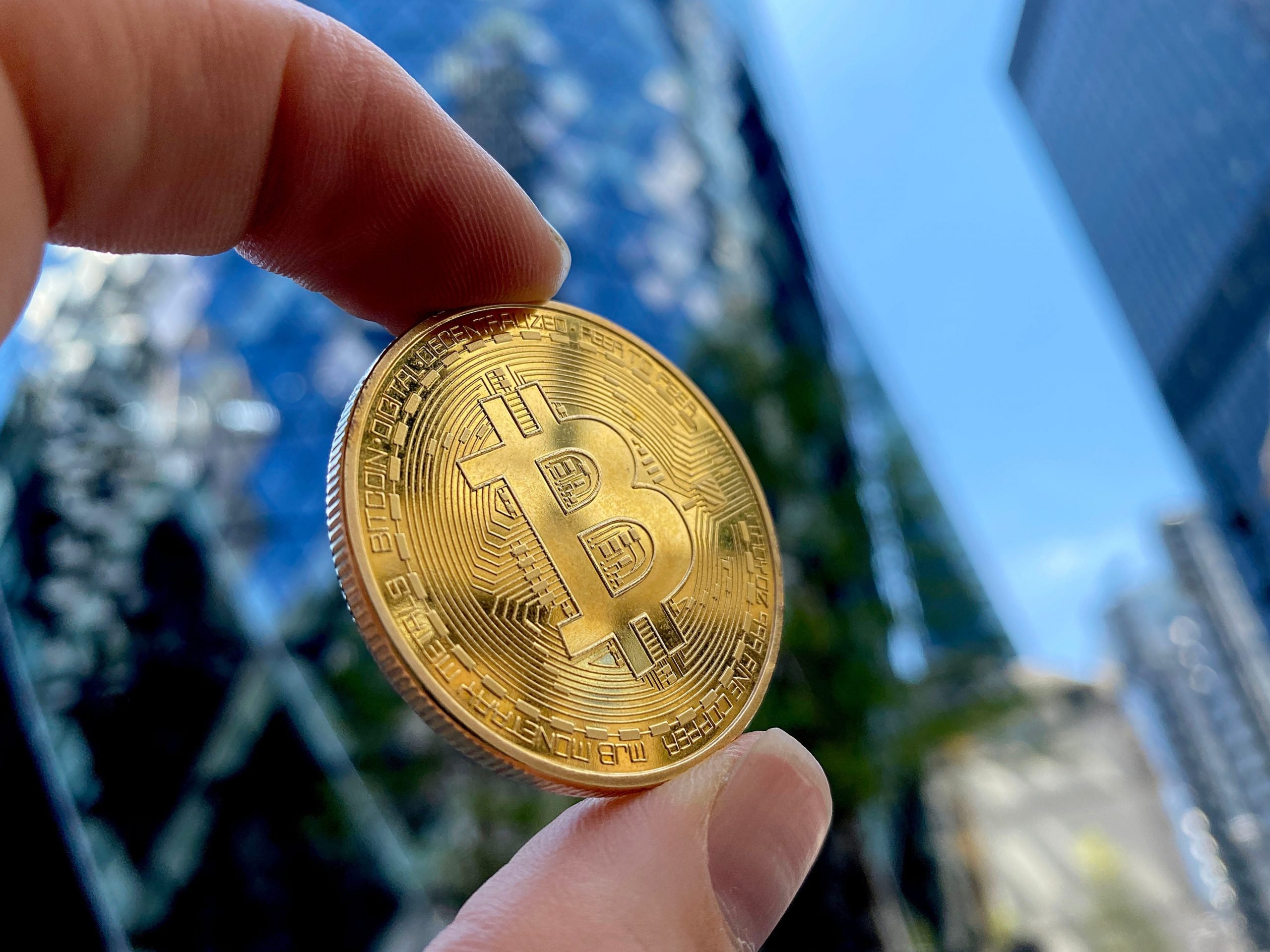 A hand holds a bitcoin toward the sky in this photo representation of the cryptocurrency.