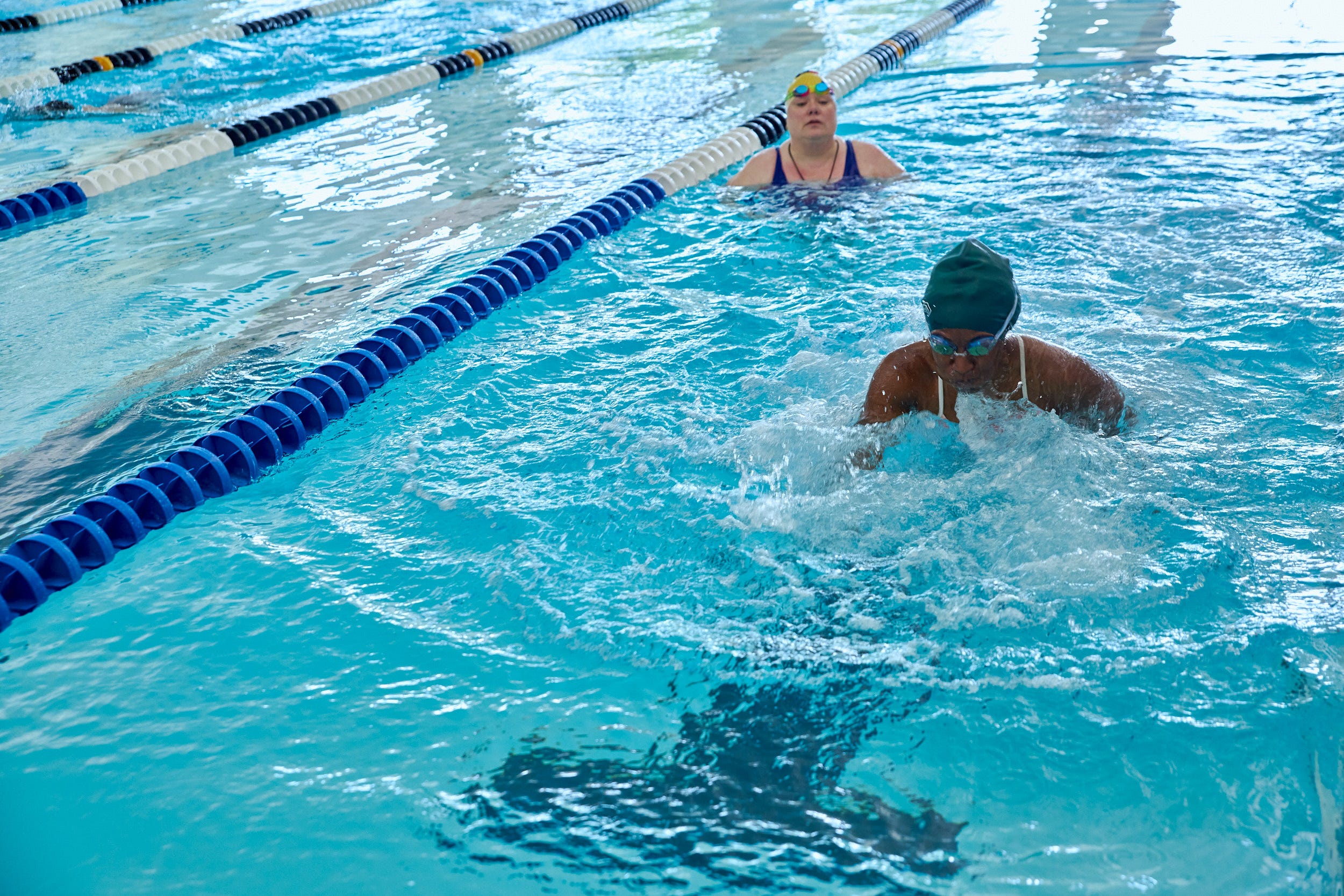 A woman swims down one lane of the pool while another looks on.