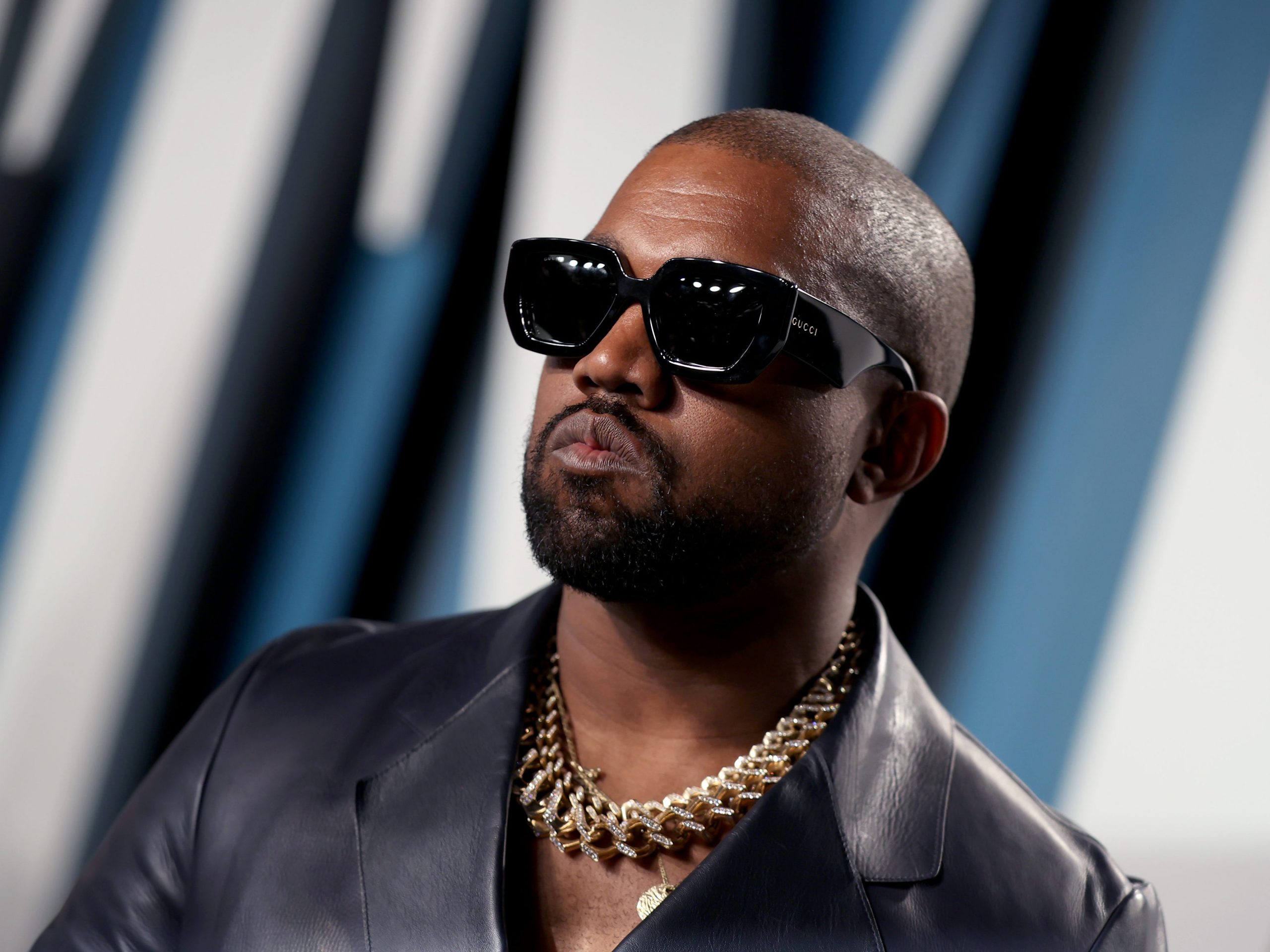 Kanye West wears sunglasses and a gold necklace at an event.