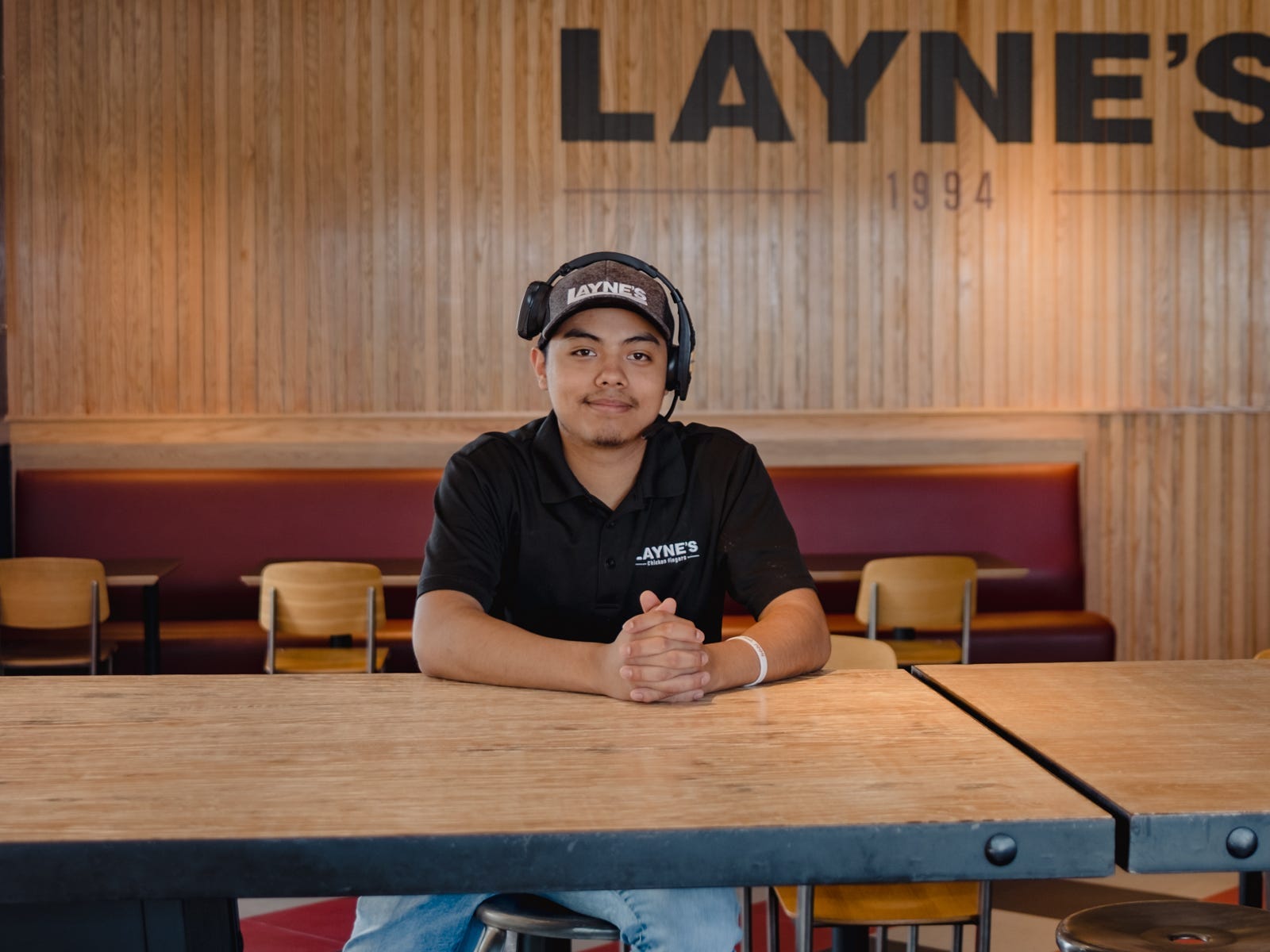 Fast-food boss Jason Cabrera sits at a long wooden table wearing a black shirt and smiles.