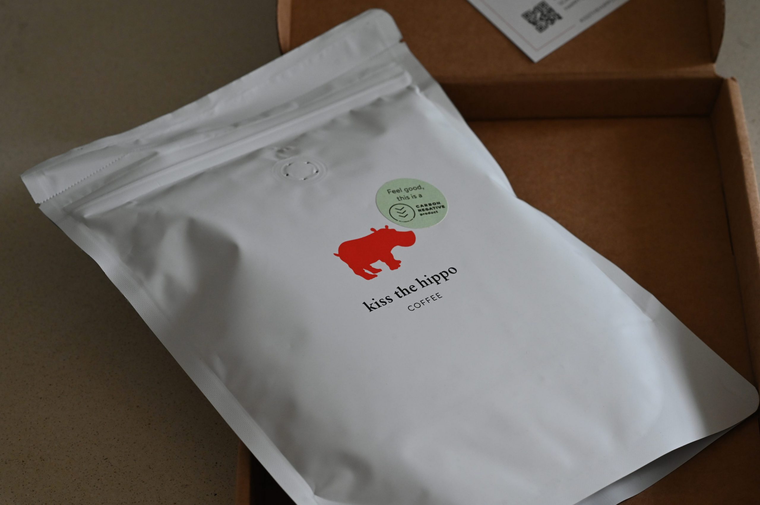 A cardboard box with a bag of Kiss the Hippo coffee with a red hippo logo