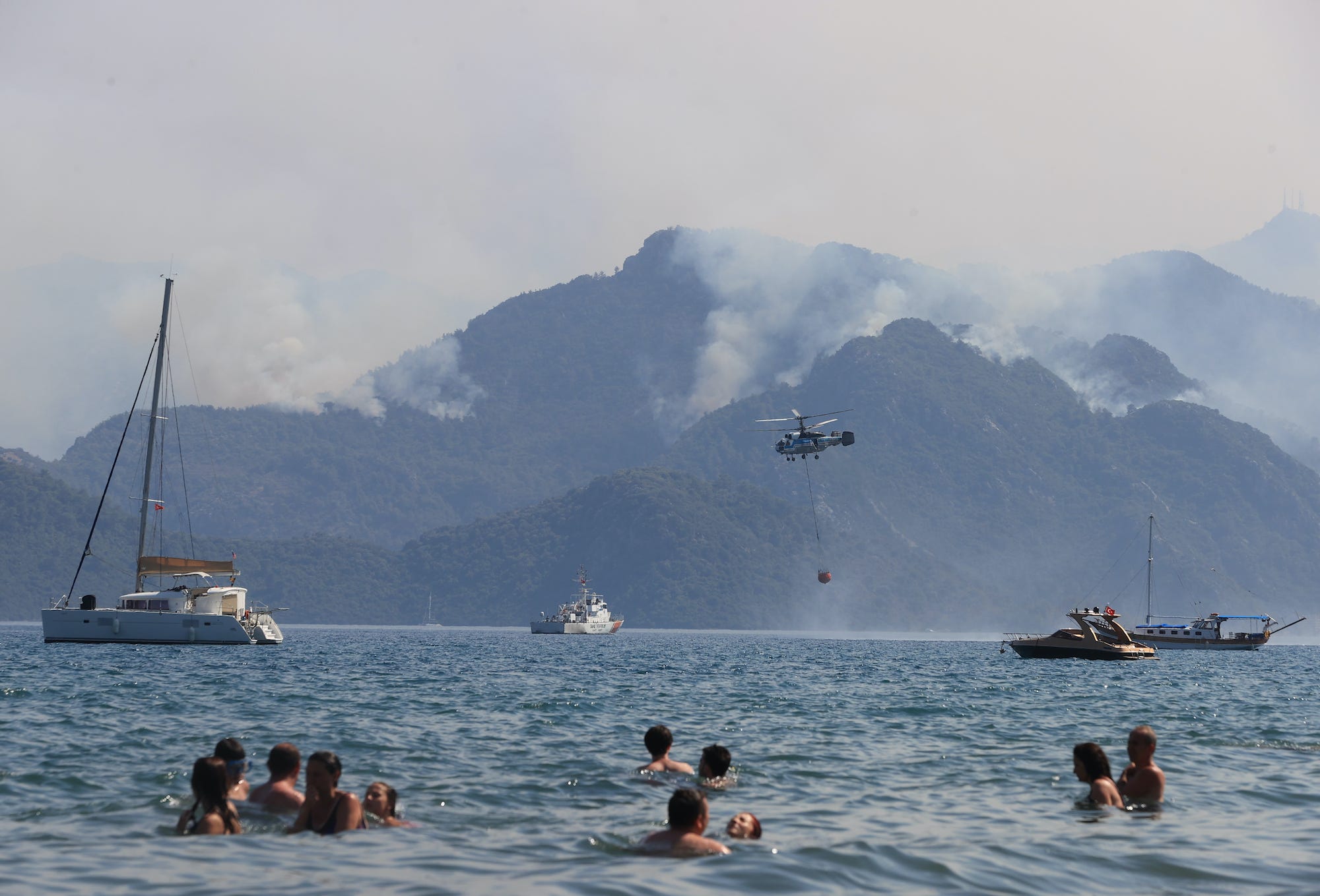 People in the water looking at a hill with smoke rising