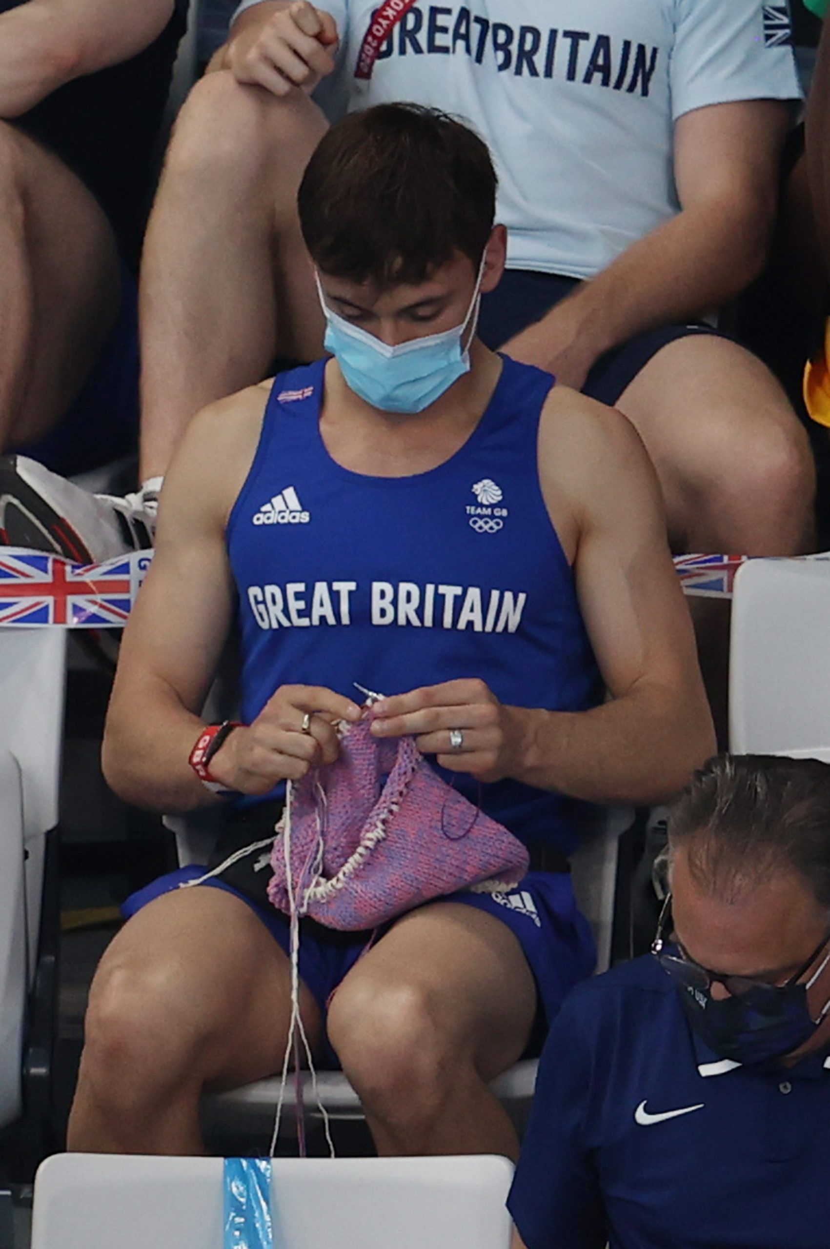 Tom Daley sits in the Tokyo Olympic spectator stands and knits.
