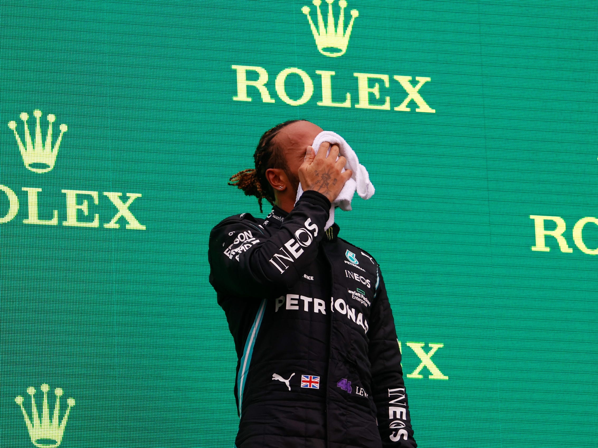 racer lewis hamilton wipes face with a towel while standing on a podium