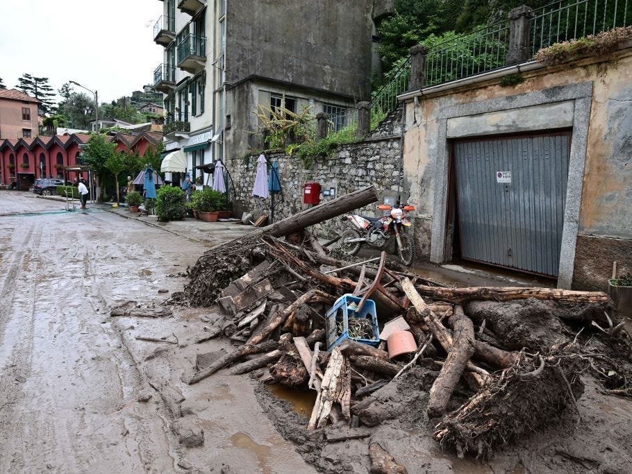 Trees and debris cover a muddy street in a village surrounding Lake Como, Italy. The damage is due to flooding and landslides caused by extreme weather.
