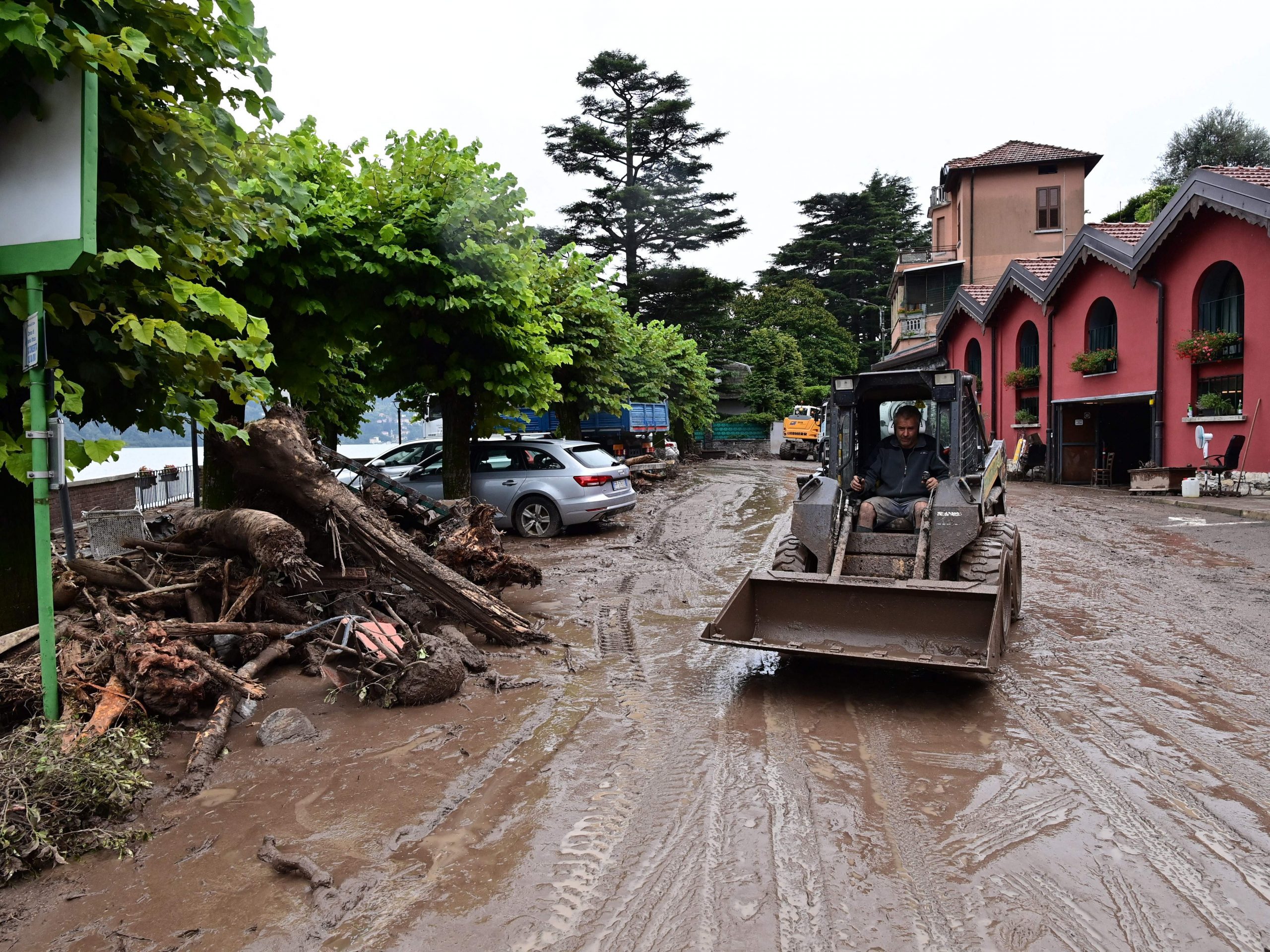 A man uses a bulldozer to clear debris on a muddy, damaged street in Laglio, Italy, near Lake Como, following extreme rainfall that caused flooding and landslides.