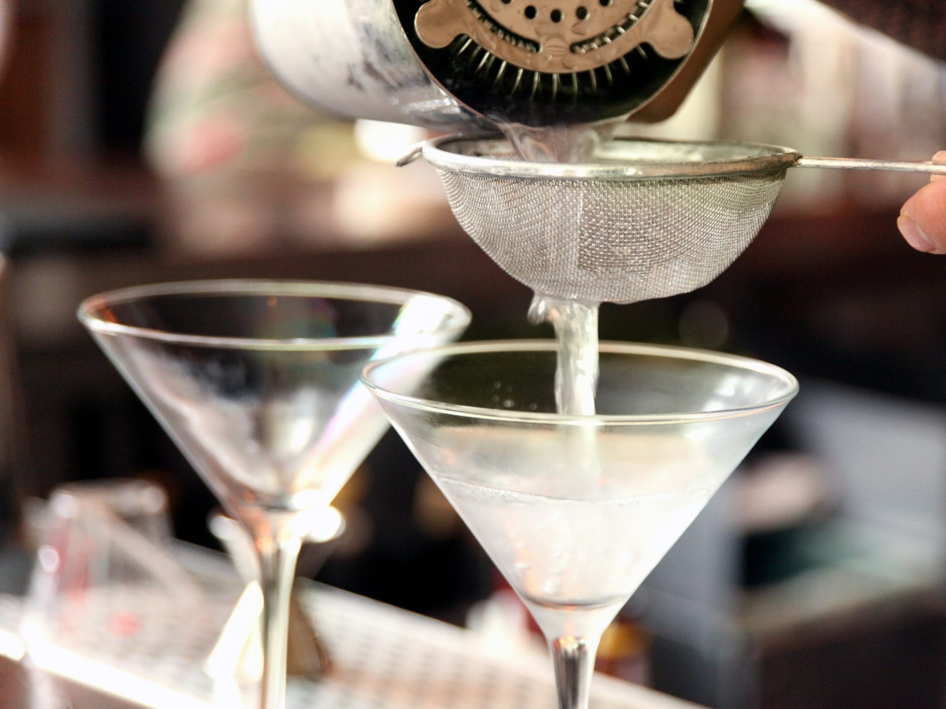 A bartender pouring a martini through a strainer into a martini glass