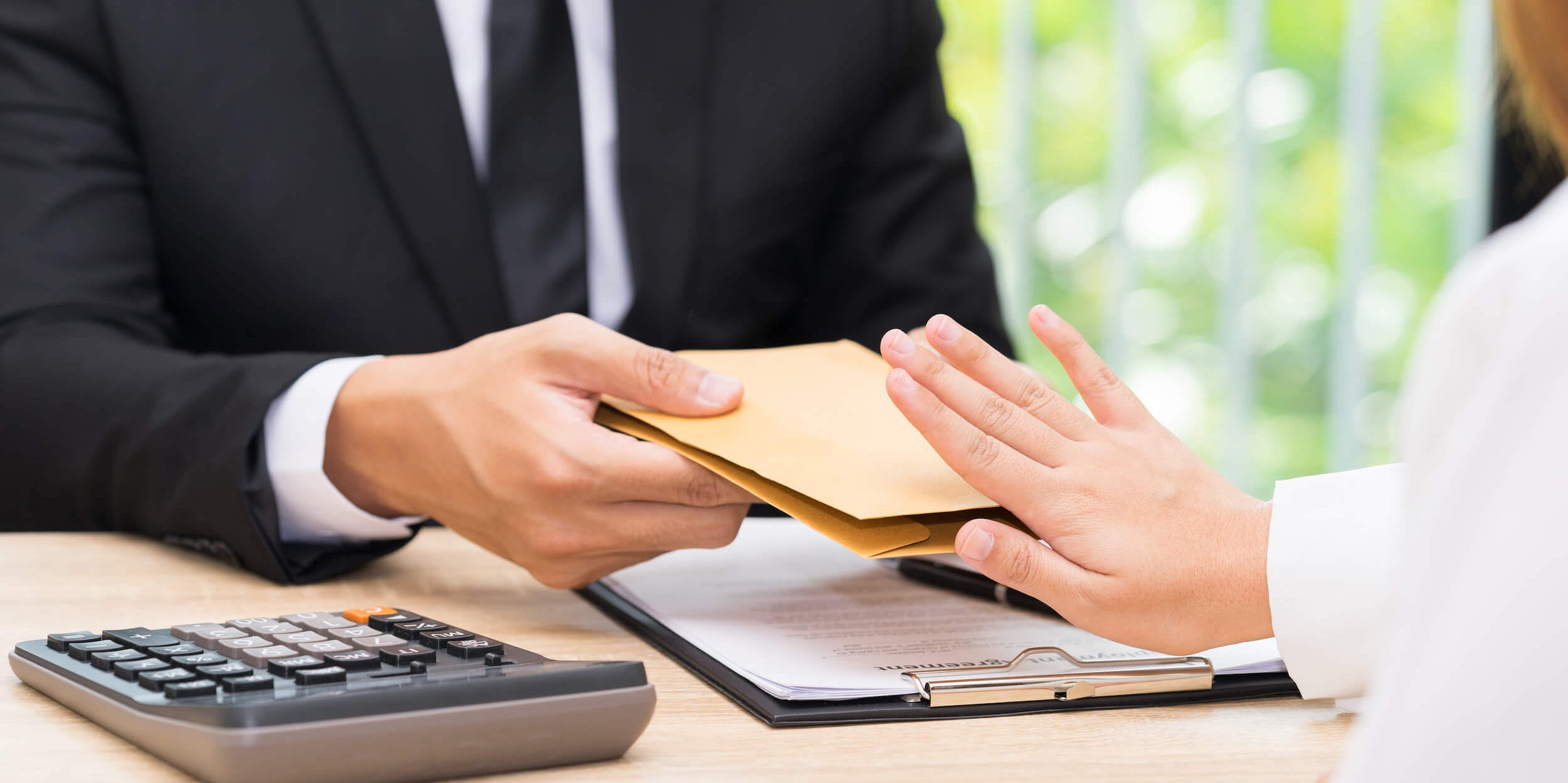 Photo showing the midsection of a woman showing a stop gesture to a businessman giving her an envelope on an office desk.