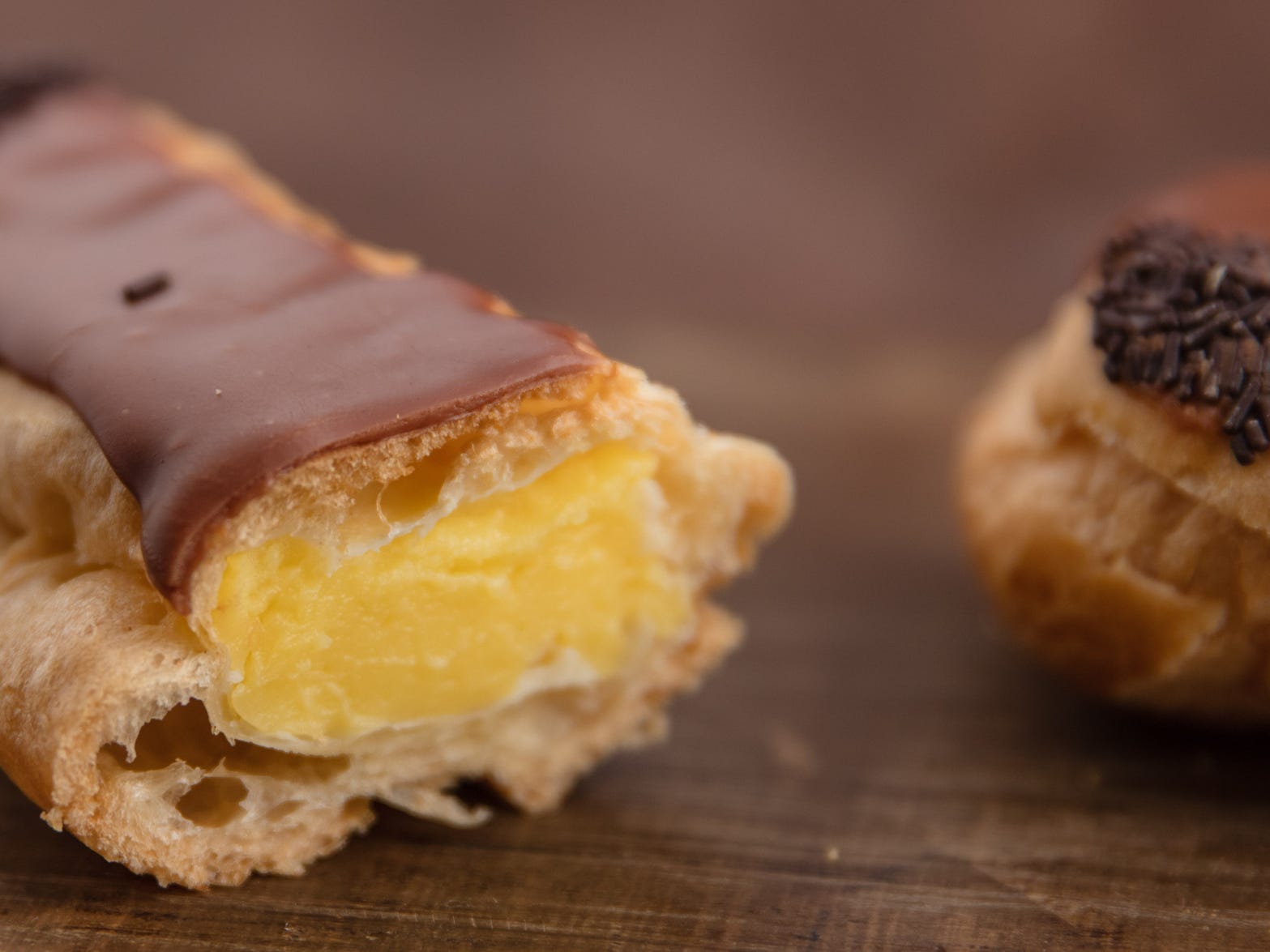 Two éclairs on a wooden cutting board.