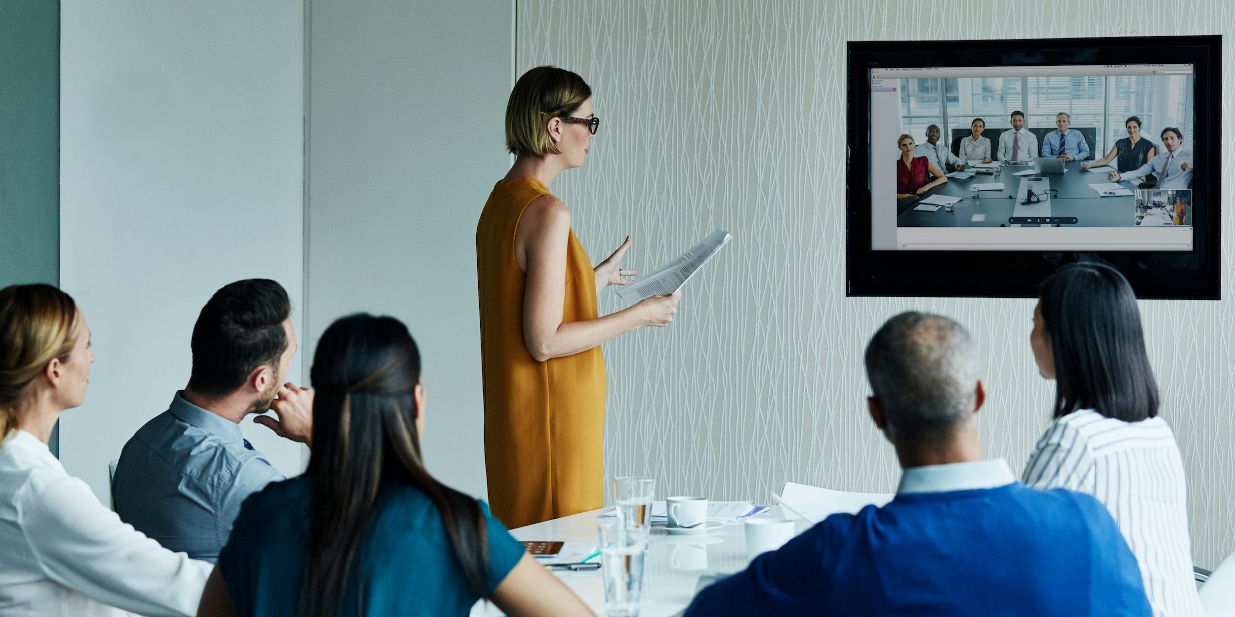 coworkers sitting in a conference call video calling with workers in another conference room