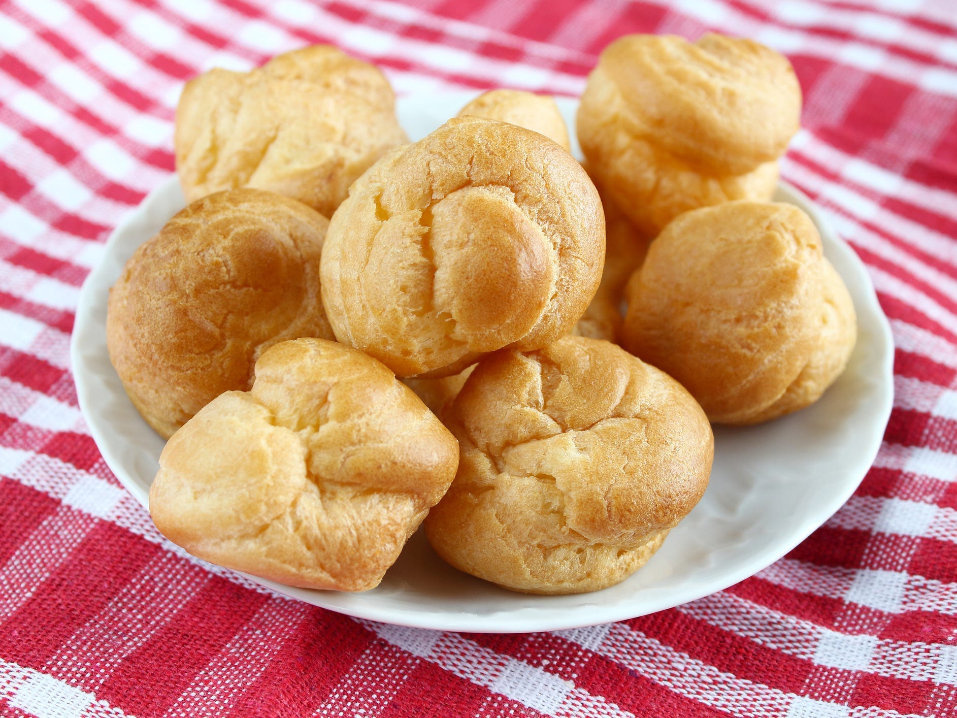 Stacked up choux pastries on a red and white checkered table cloth.