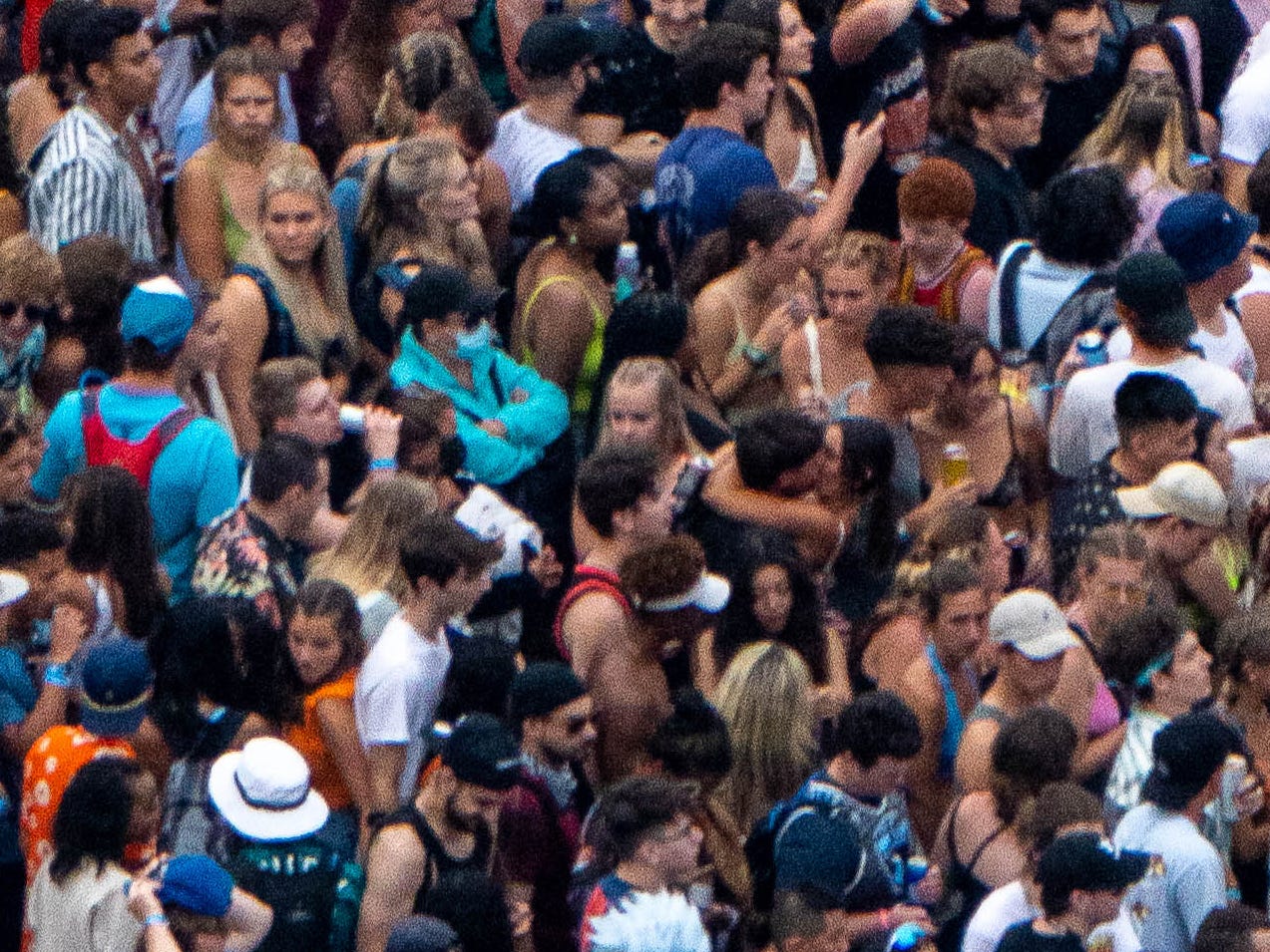 A person wearing a mask and a couple kissing at Lollapalooza 2021