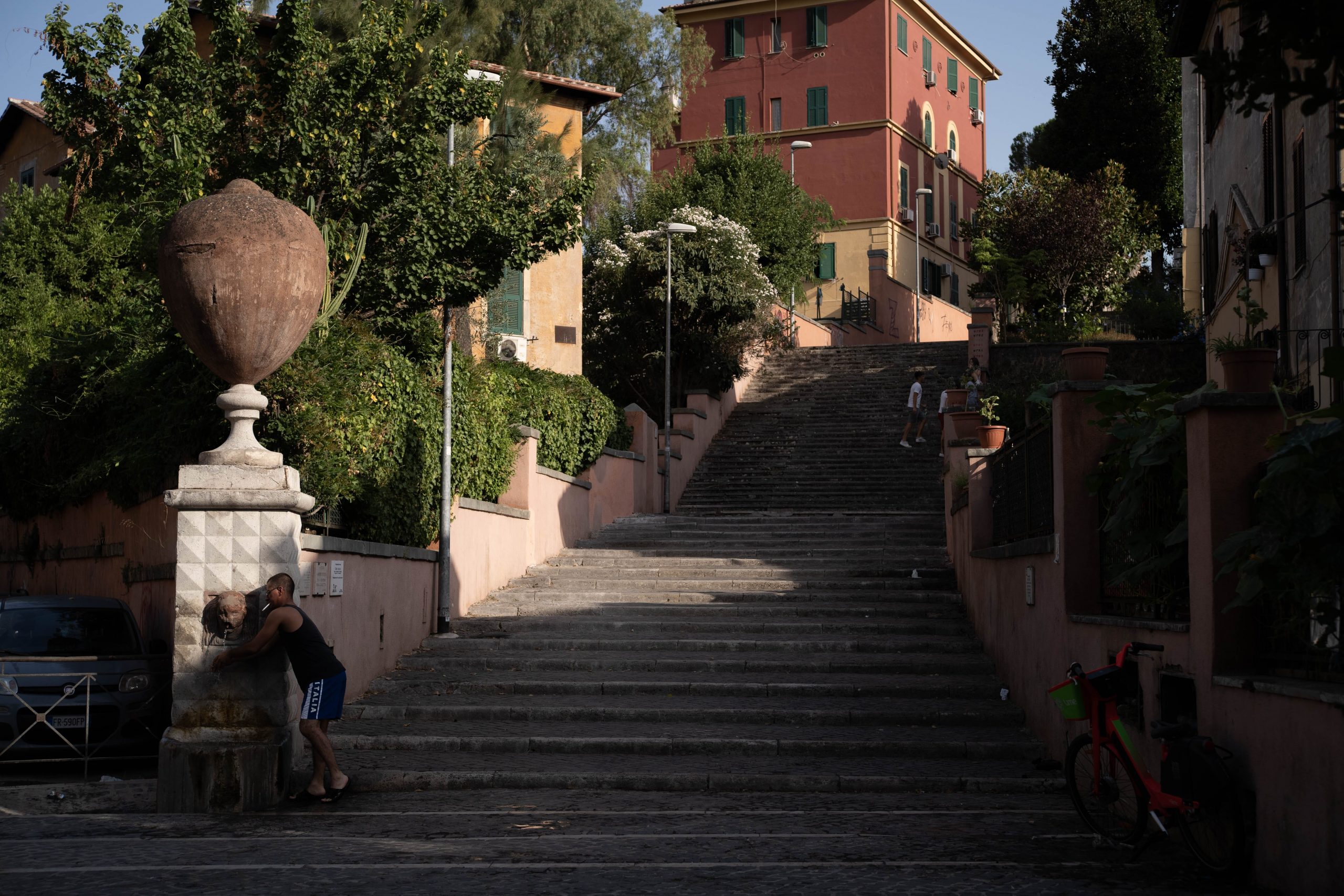 A man at a water fountain at the base of a long outdoor staircase