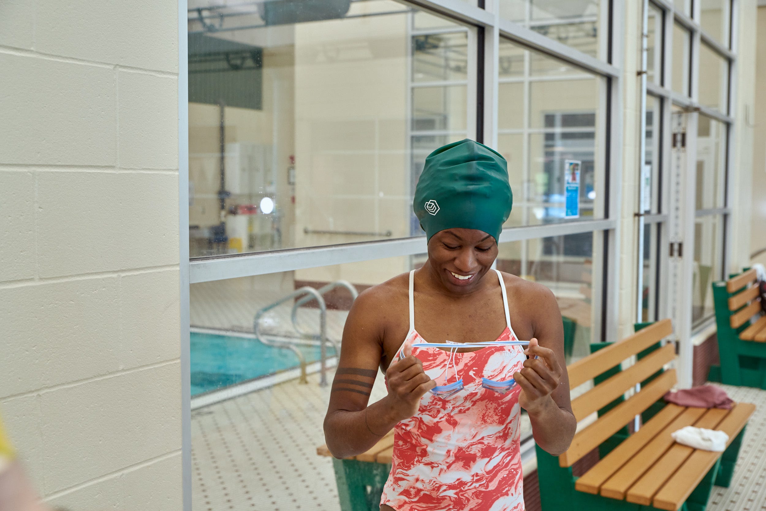 A swimmer is seen on the deck of an indoor pool preparing to put on her goggles
