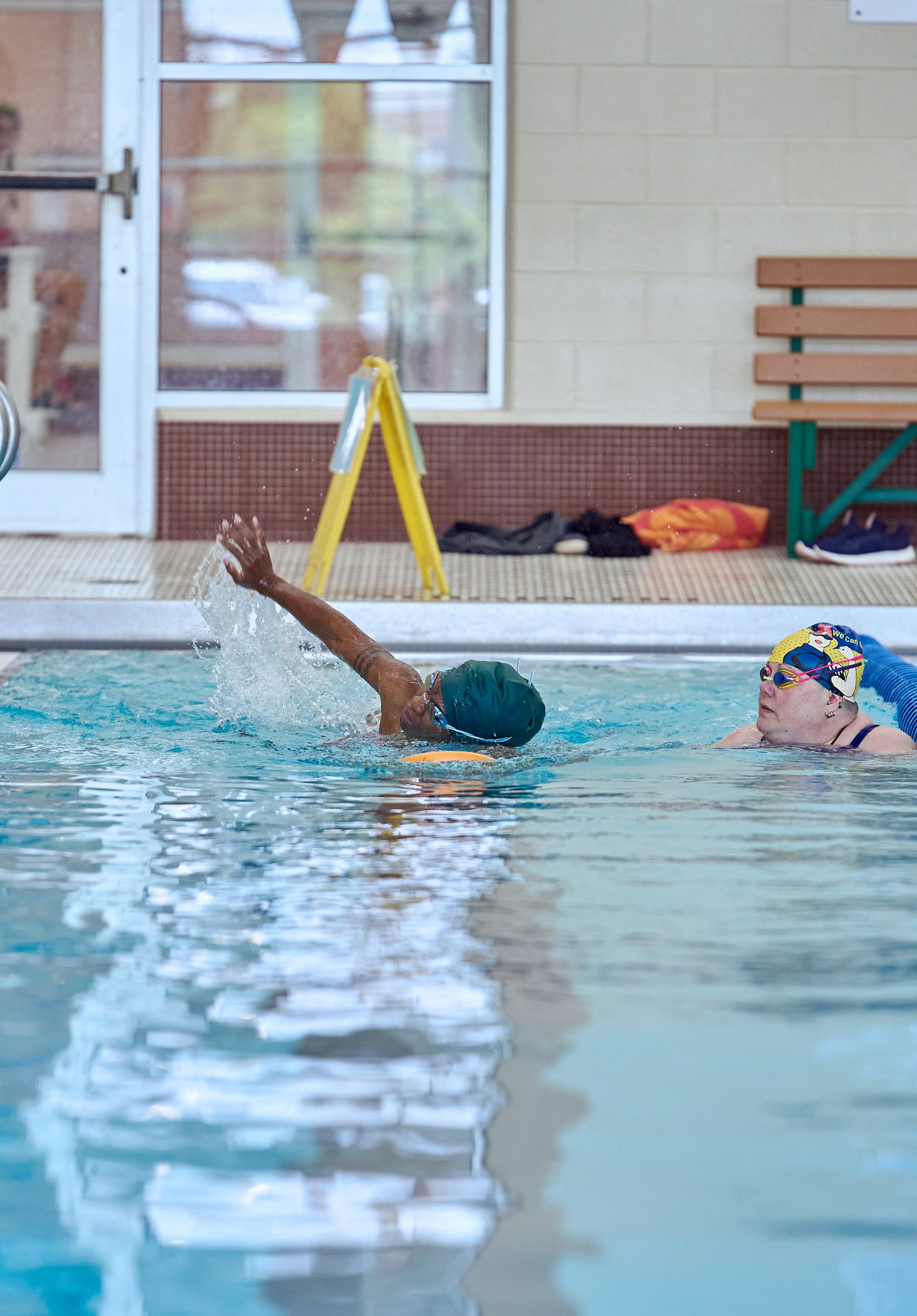 A women swims freestyle as another looks on.
