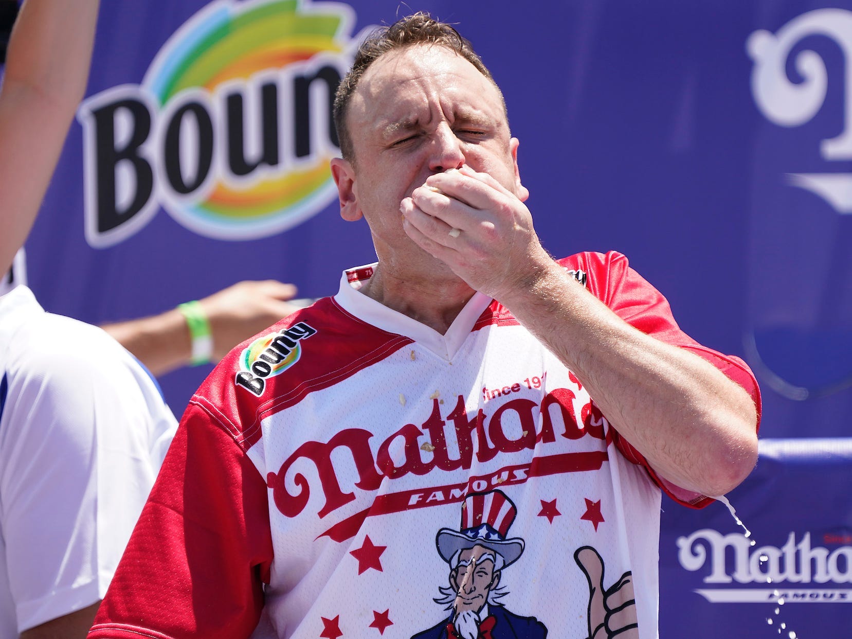 Joey Chestnut eating hot dogs during the Nathan's contest in front of a blue background.