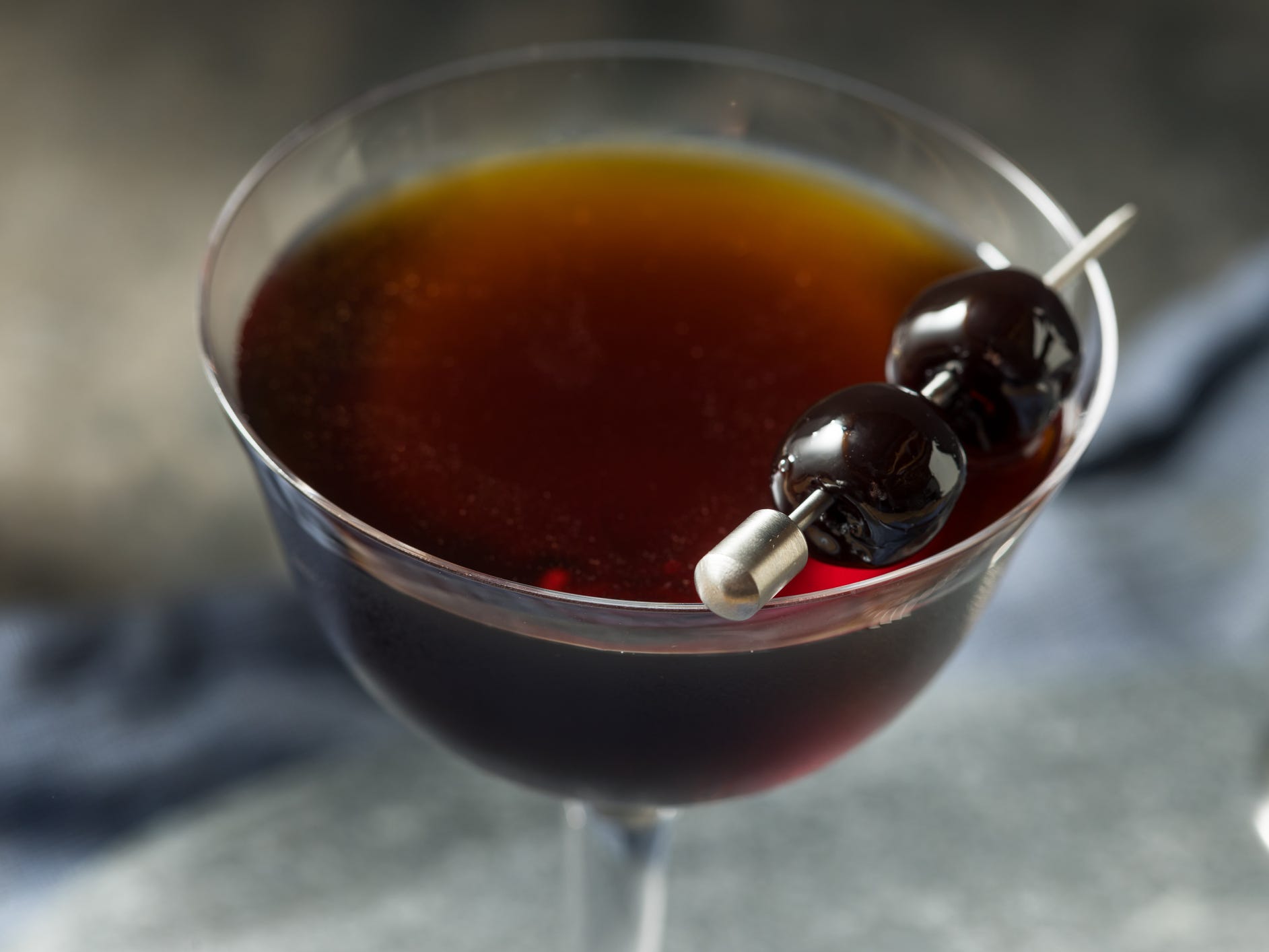 A closeup of a black Manhattan in a coupe glass garnished with two cherries